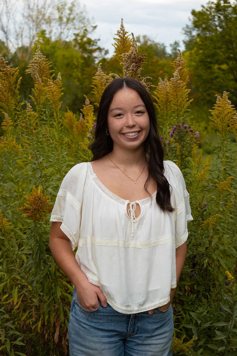 A person in a white peasant blouse stands in front of tall goldenrod plants during a summer outdoor photoshoot.
