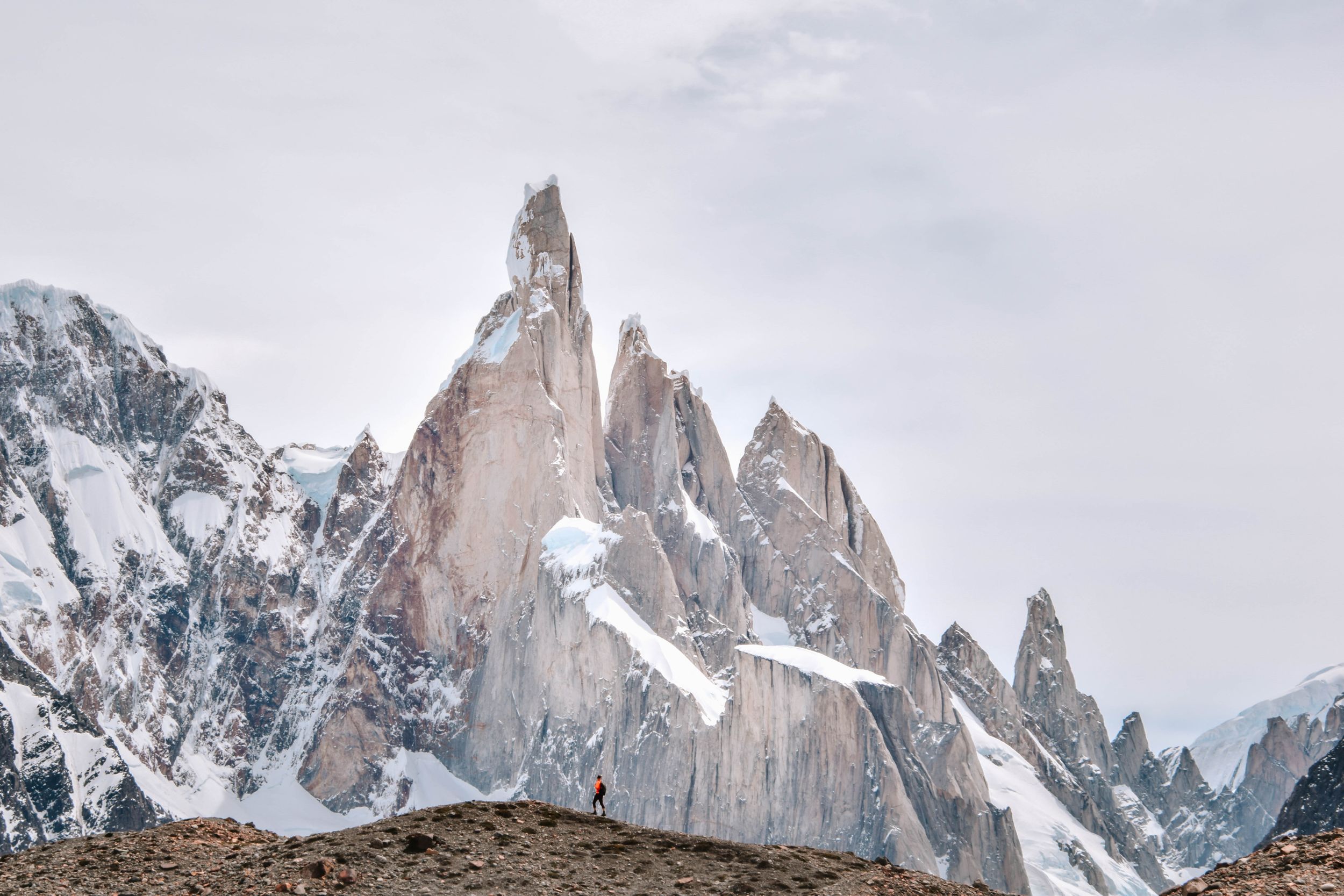 Snow-capped mountain peaks rise dramatically against a cloudy sky in this panoramic landscape view.