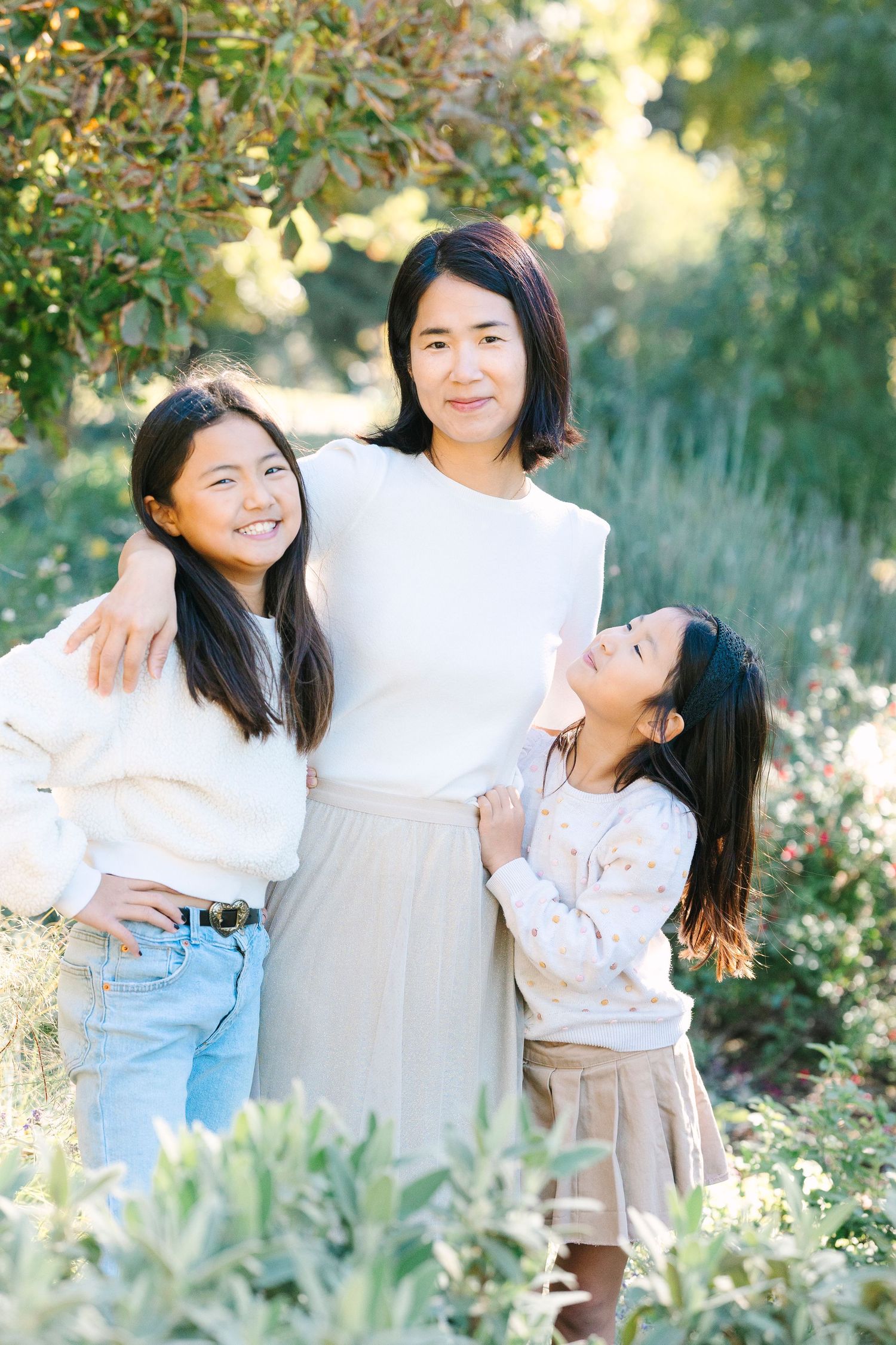Three people share a candid moment together outdoors in coordinated white outfits.