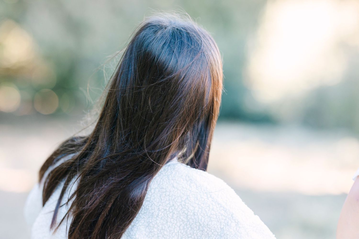 Long dark hair flows in the sunlight against a soft blurred natural background.
