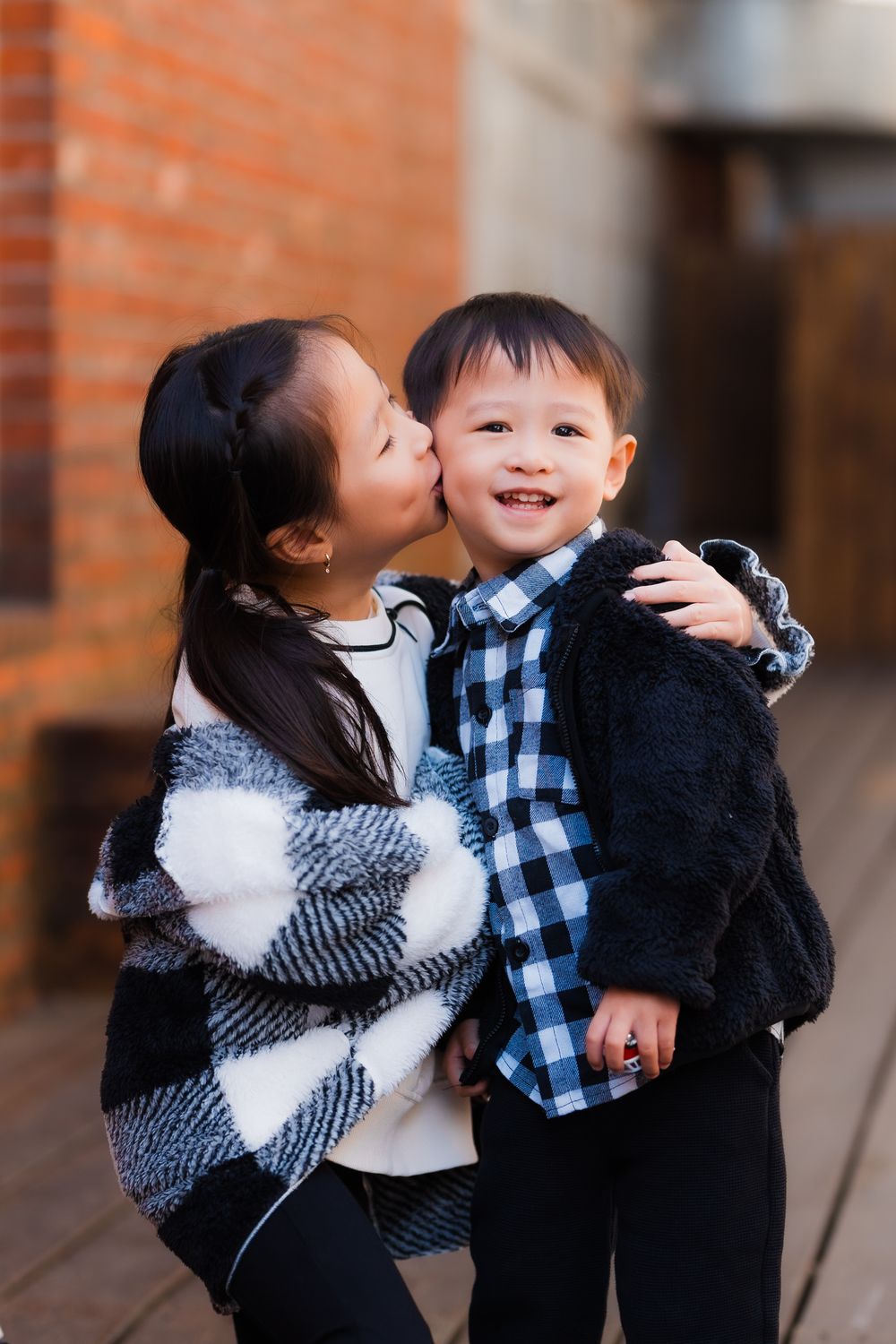 Two young children sharing a sweet moment in checkered blue and white plaid outfits in and artistic industrial creative park.