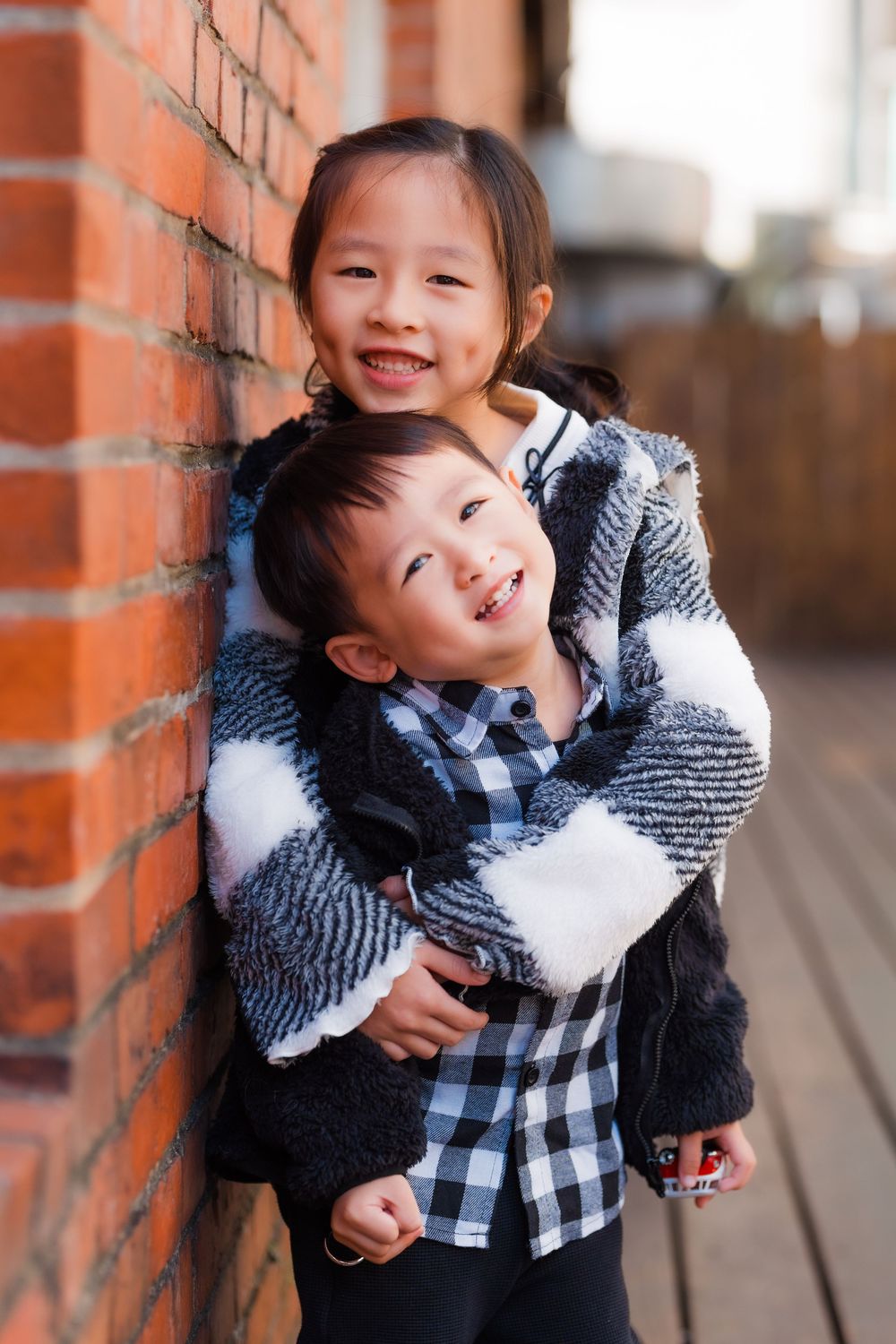 Brother and sister smiling and posing with a hug next to a brick wall