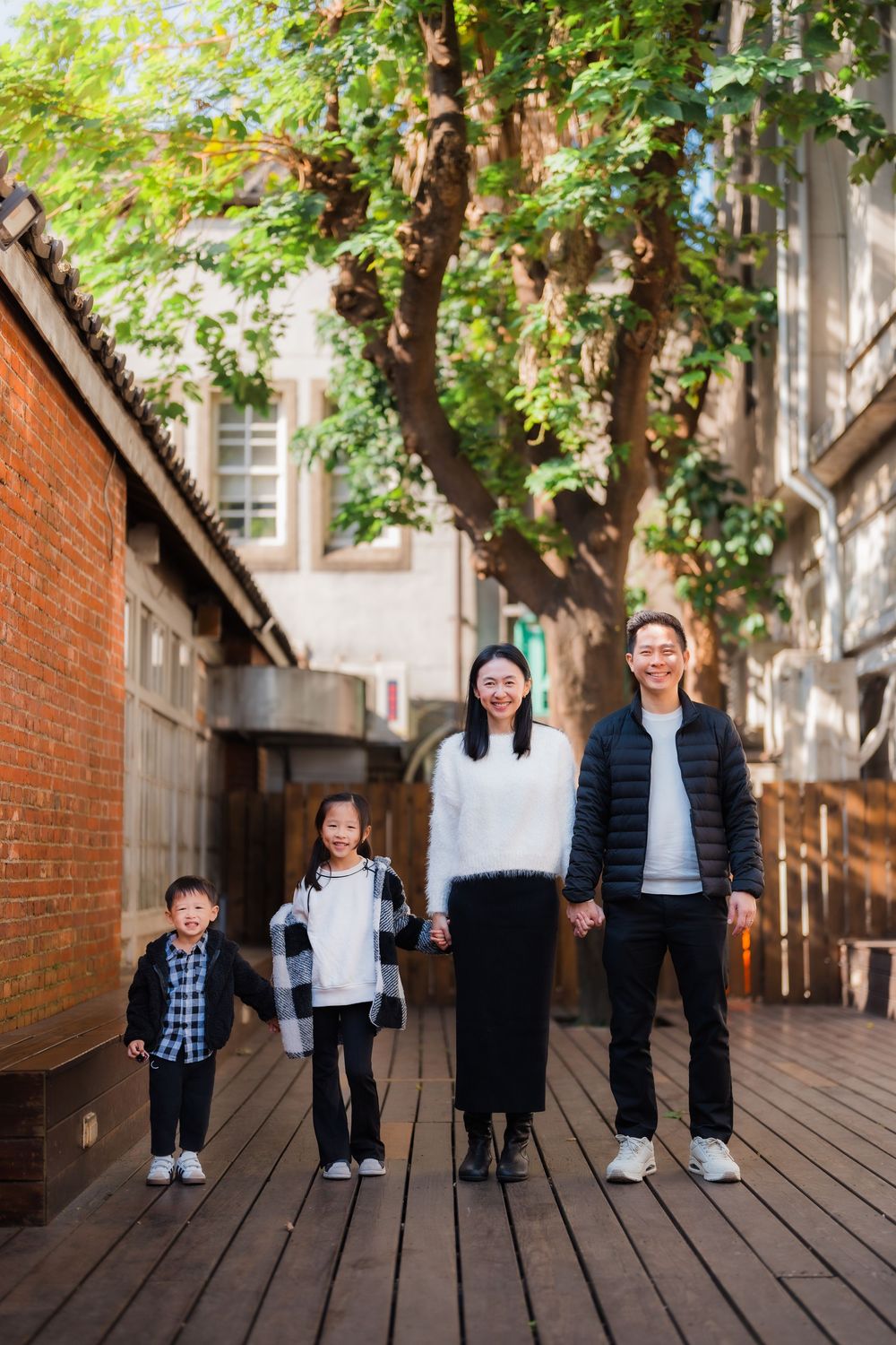 A family standing side by side holding hands on a shaded outdoor deck next to a brick wall at Huashan Creative Park