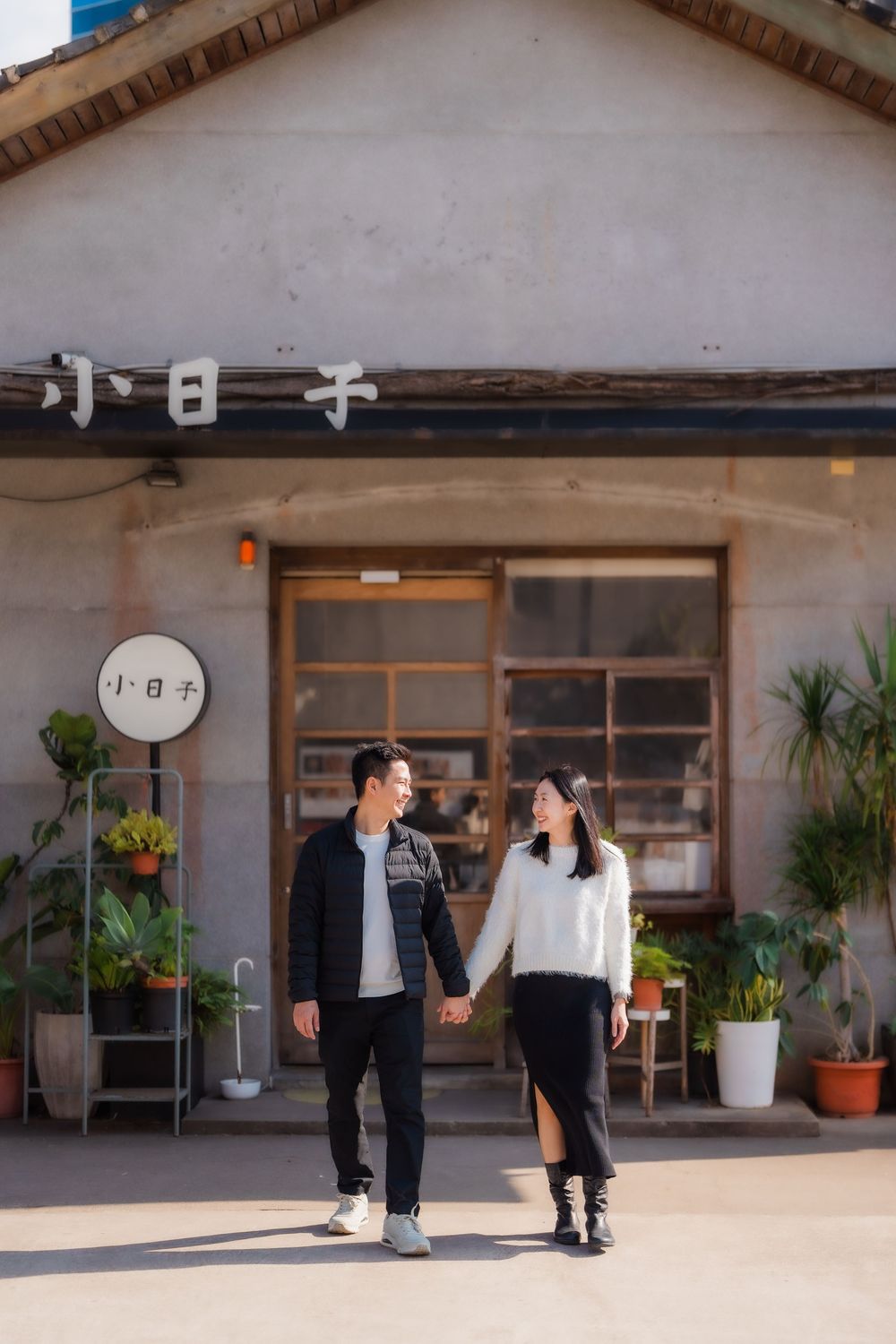 A couple enjoys a romantic walk holding hands at golden hour in front of a Japanese style shop in Huashan 1914 Creative Park in Taipei.