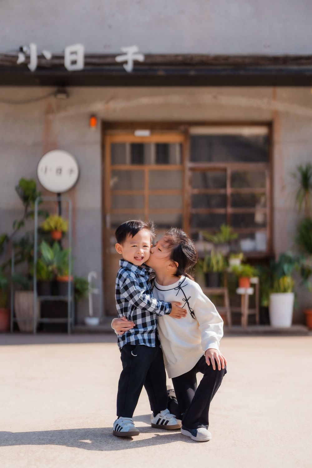 A younger brother receives a kiss from his sister at Huashan 1914 Creative Park in front of a cute Japanese style shop.