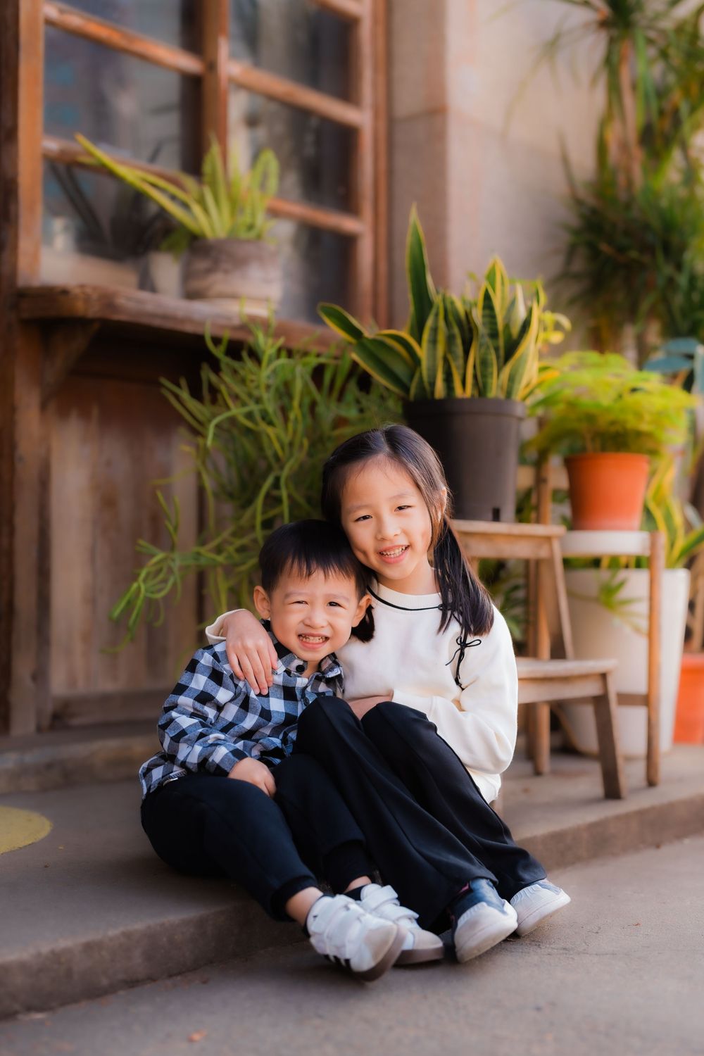 Two playful siblings share a laugh sitting on a modern rustic store front stoop.