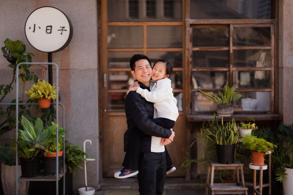 A precious moment of a father holding his daughter close in front of a modern wooden Japanese style shop in Taipei, Taiwan