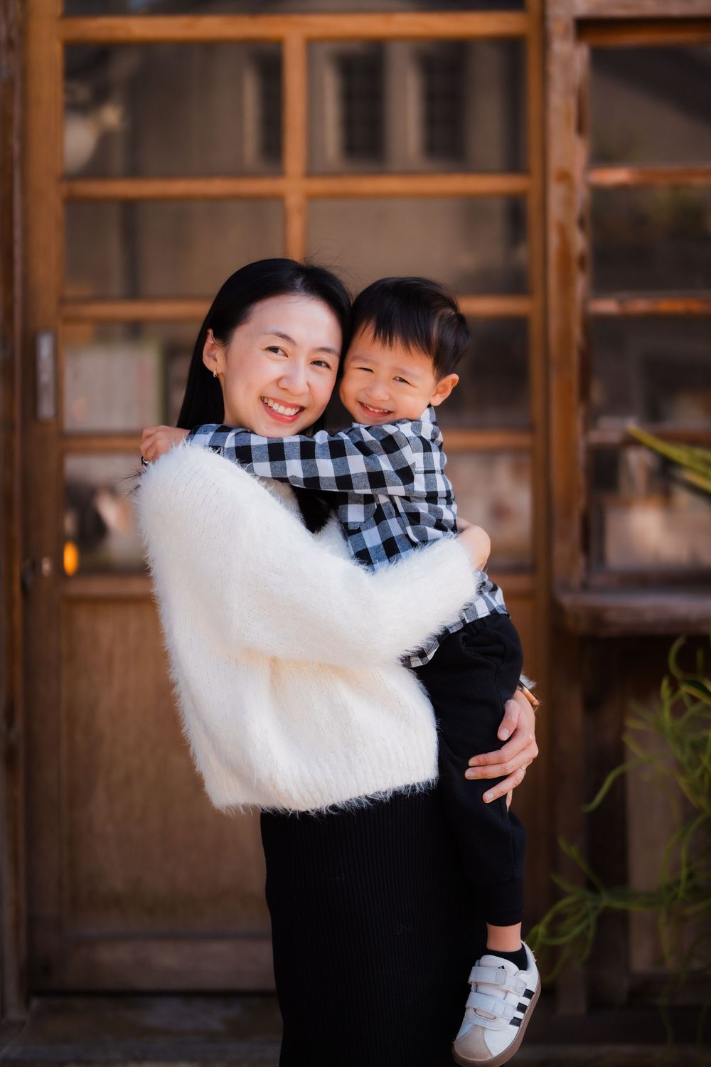 Adorable moment of a mom holding her young son by a glass and wooden door in Taipei's Huashan 1914 Creative Park.