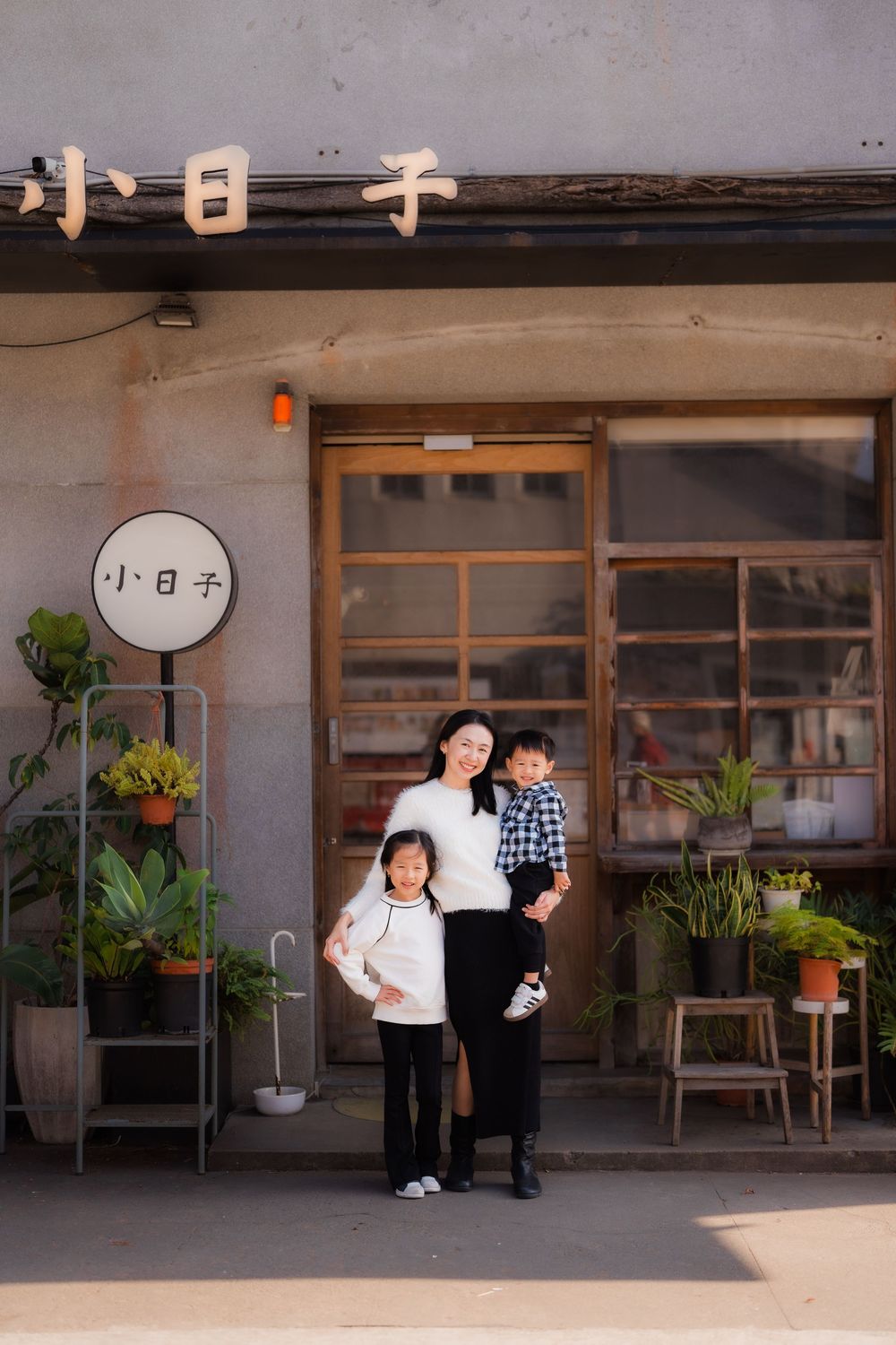 Mom and her two children pose for a photo by a minimalist Japanese building with wooden elements and potted plants at Huashan Creative Park