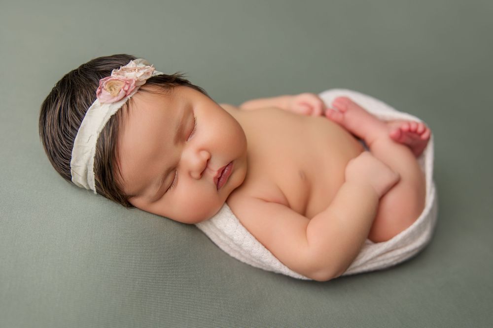 Sleeping newborn baby in white beanie against muted olive green background.