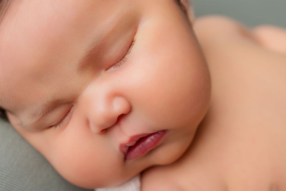 Close-up artistic portrait of a sleeping baby's peaceful features against a soft neutral background.