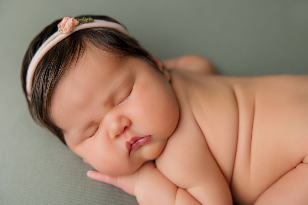 Sleeping newborn baby curled up peacefully on soft green backdrop in artistic newborn photography pose.
