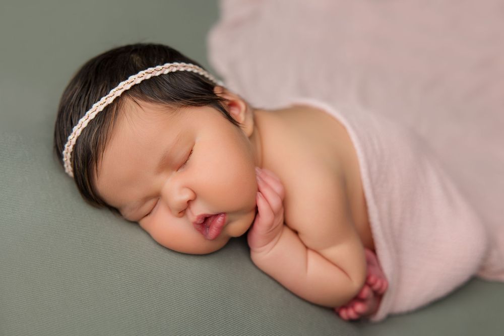 Sleeping newborn in pink wrap with lace headband during professional photo session.