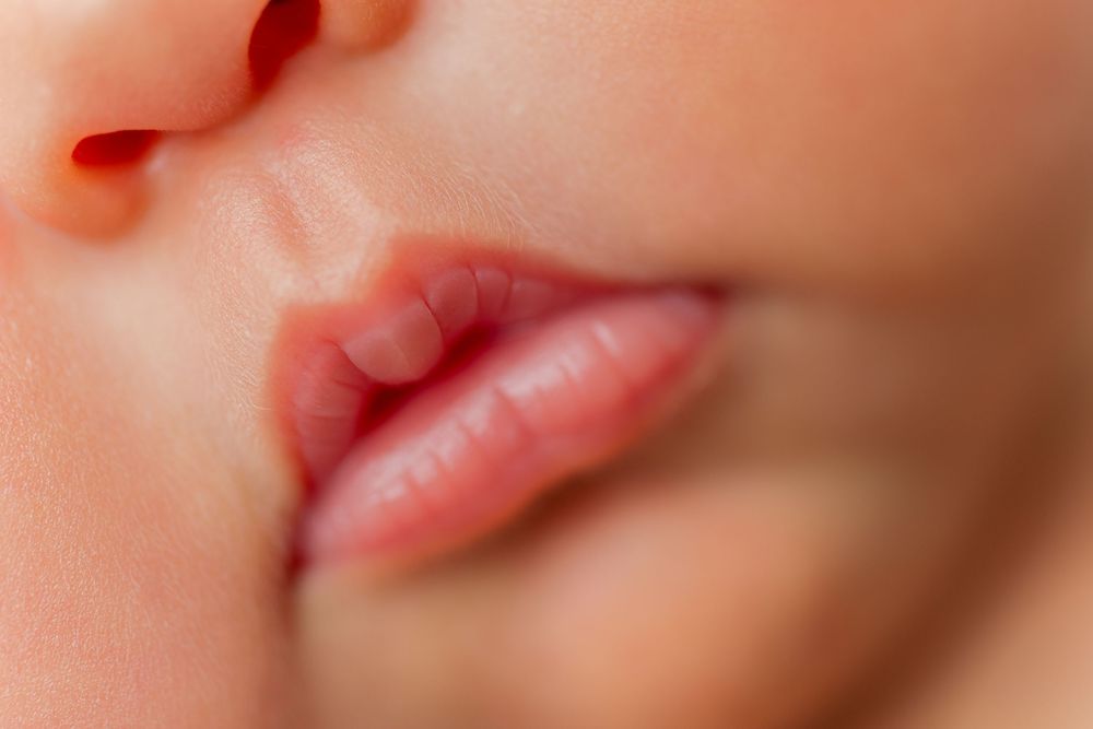 Close-up macro photograph showing the delicate pink lips of a sleeping baby against soft skin.