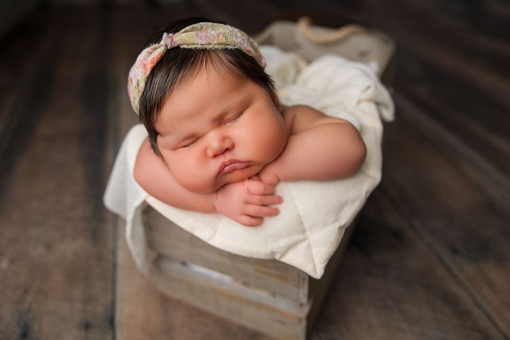Sleeping newborn in white wrap on textured dark wood surface.