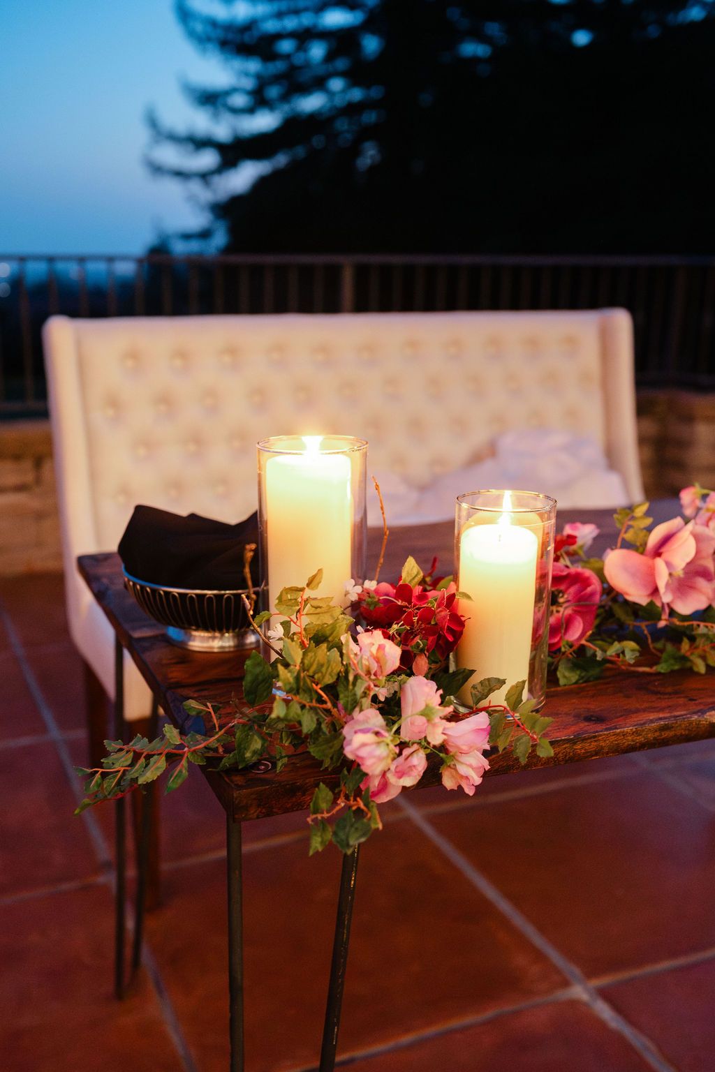 Elegant table settings with name cards and floral centerpieces featuring pink and white ranunculus flowers and glowing candles.