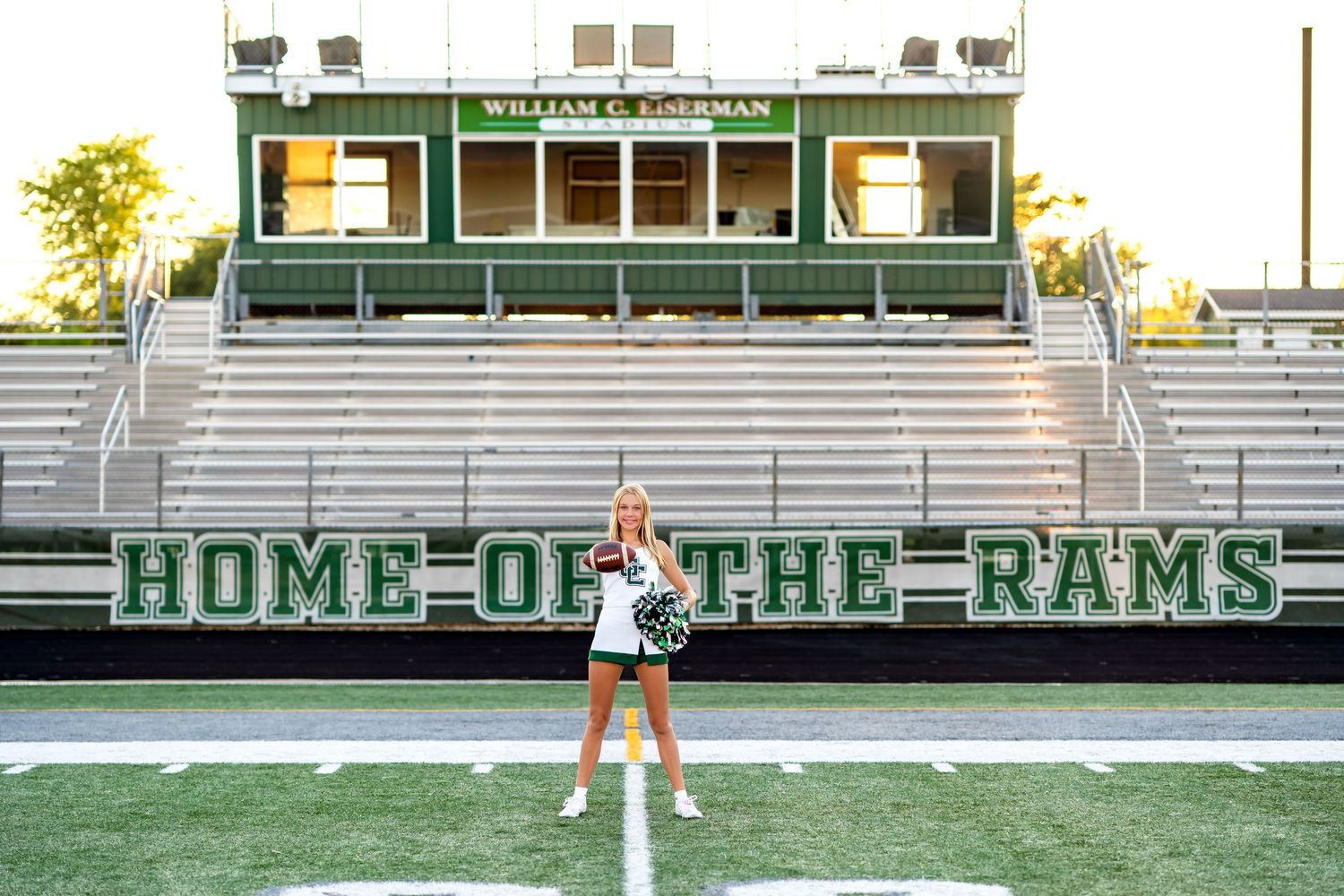 High school bleachers and stadium seats display 'Home of the Rams' sign with cheerleader practicing routines on field.