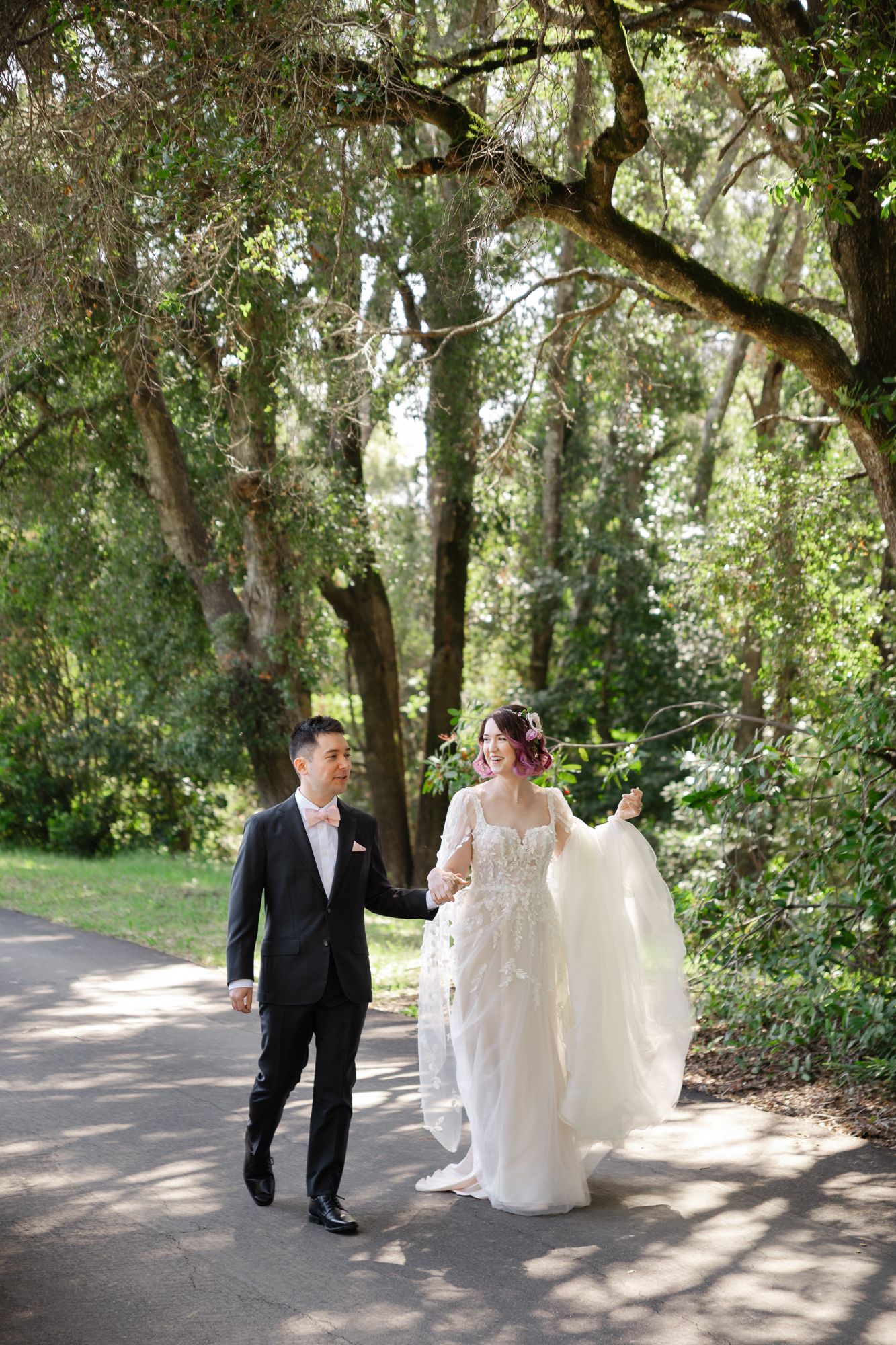 Wedding couple walking together along a tree-lined path in a romantic outdoor woodland setting.