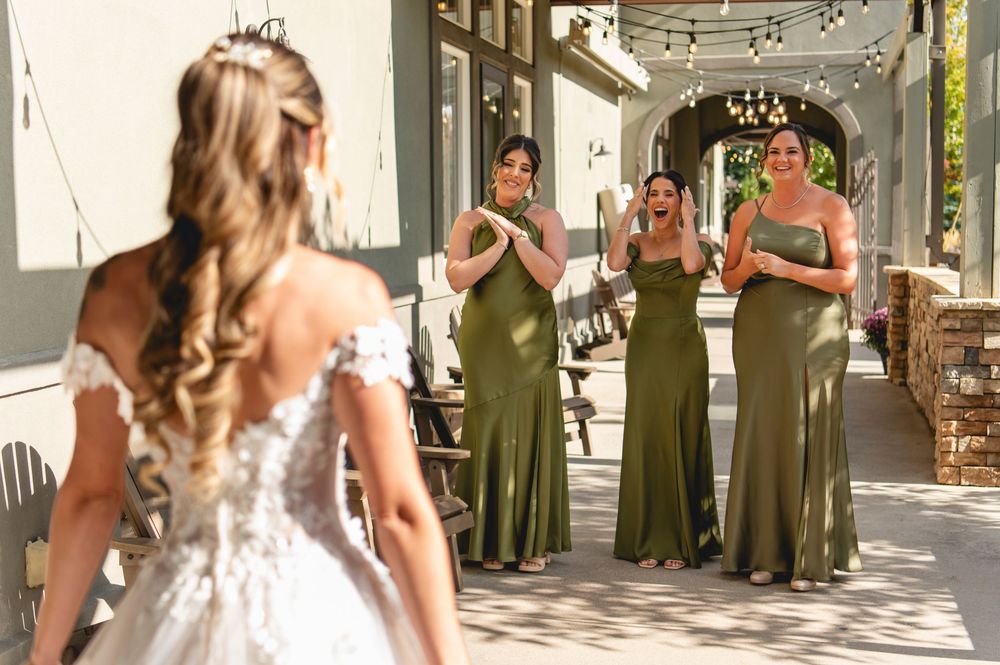 Bride in lace dress surrounded by bridesmaids in olive green dresses during emotional first look moment.