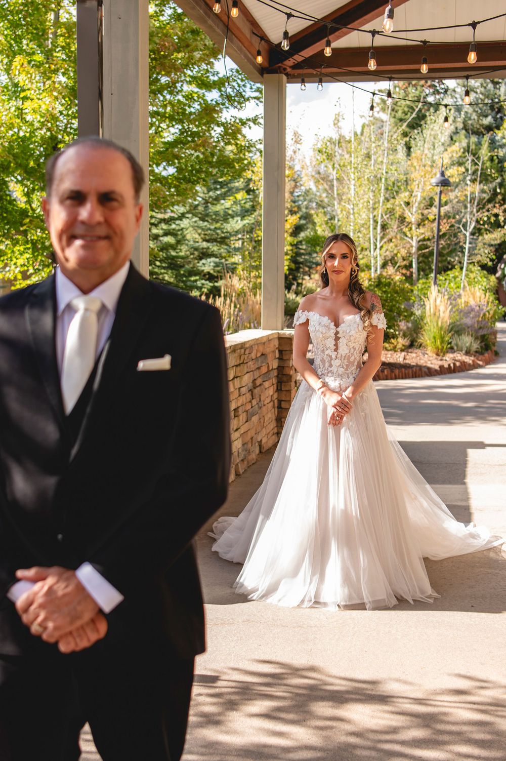 Emotional first look moment between bride and father on covered porch with string lights overhead.