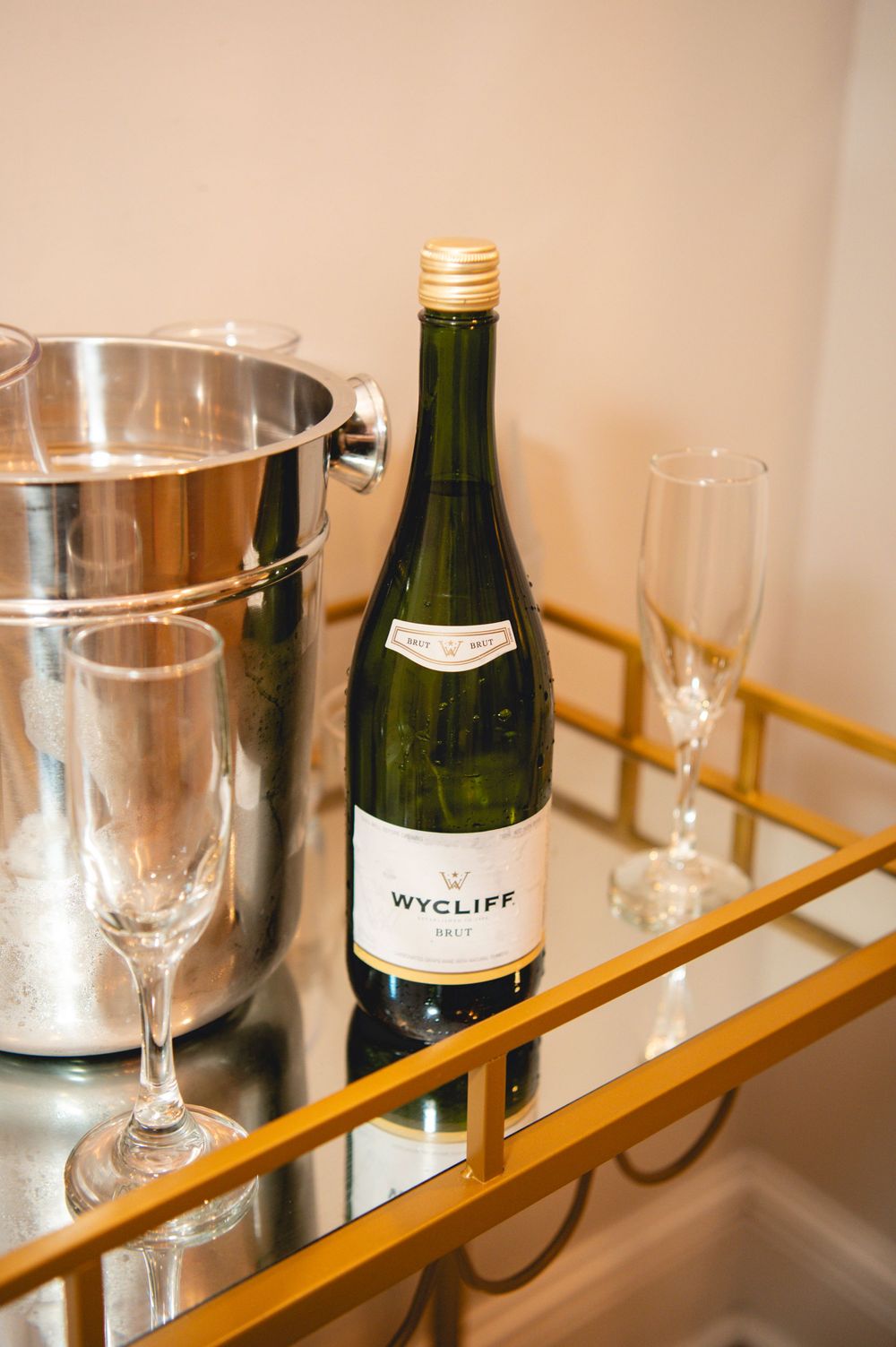 Elegant wine setup with champagne bottle, crystal glasses, and ice bucket arranged on a gold-trimmed mirrored surface.