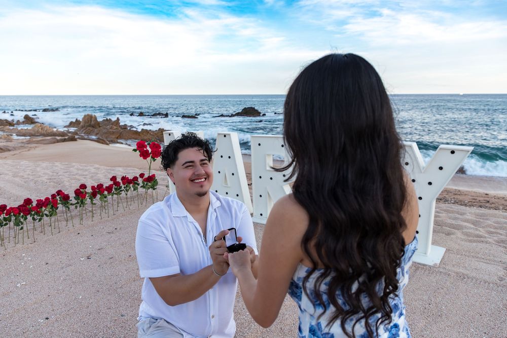 A couple shares a romantic moment on a beach during a seaside photo session with ocean waves in the background.