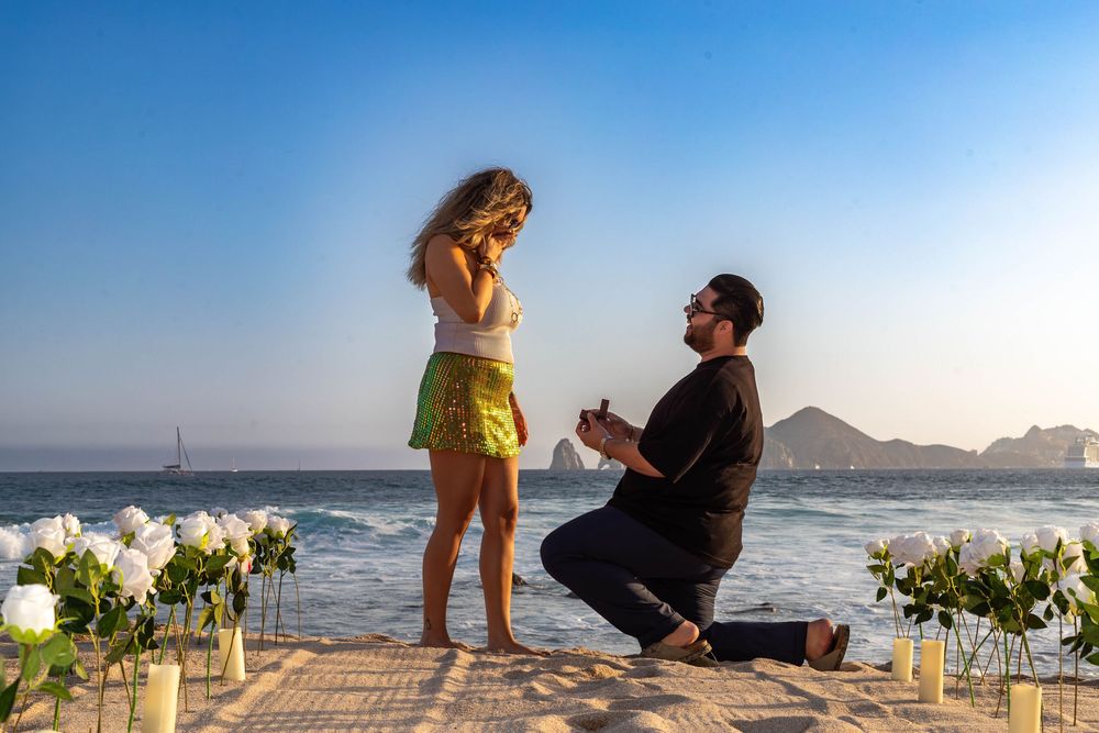 A romantic beach proposal setup with flowers and candles at sunset by the ocean.