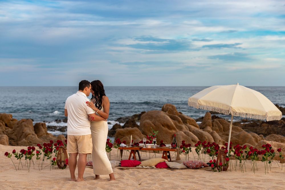 A romantic beach wedding scene with white umbrellas and chairs set up along the sandy shoreline at sunset.