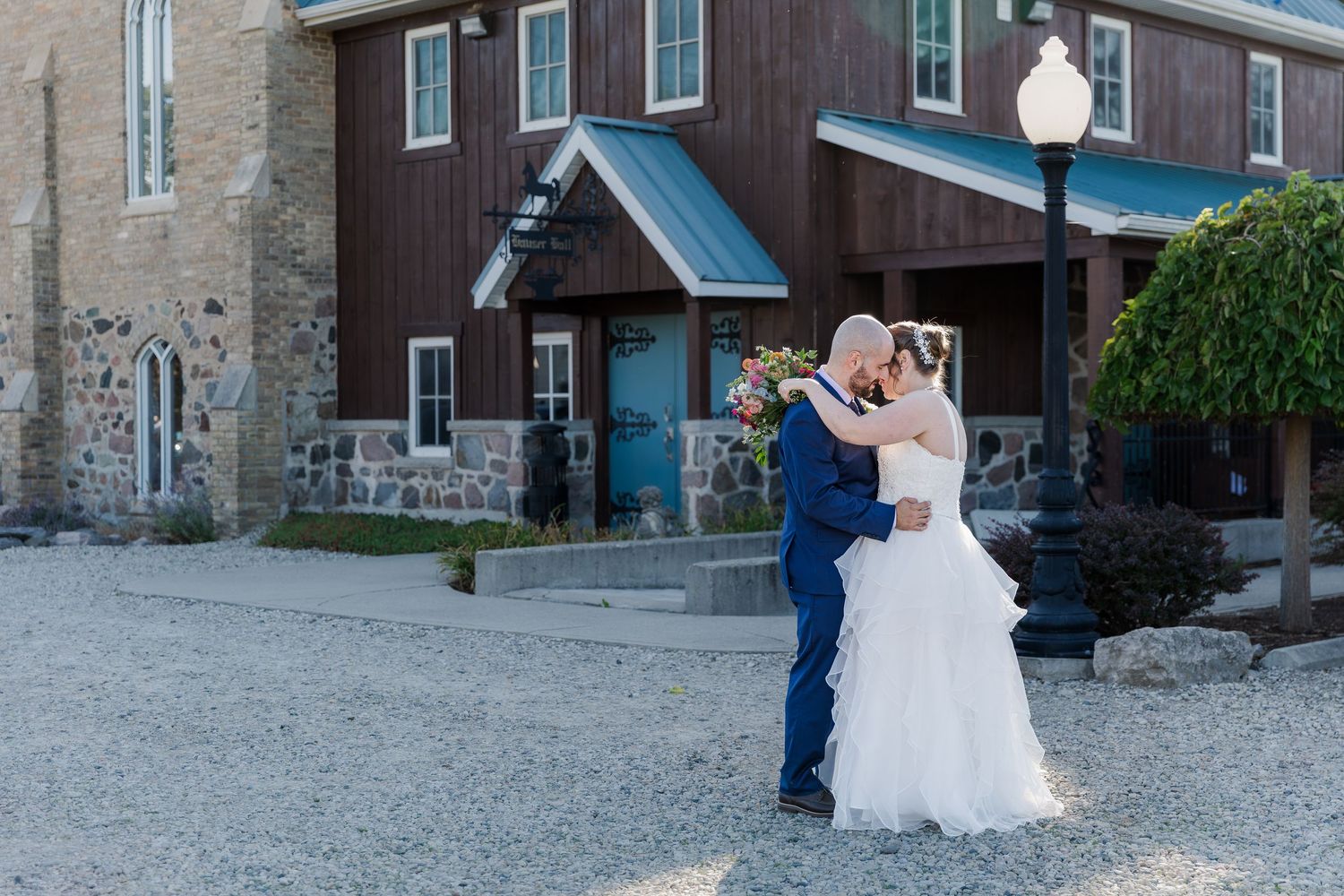 Bride and groom embrace in front of the historic stone and wood building at Hauser Hall in Kitchener, Ontario.
