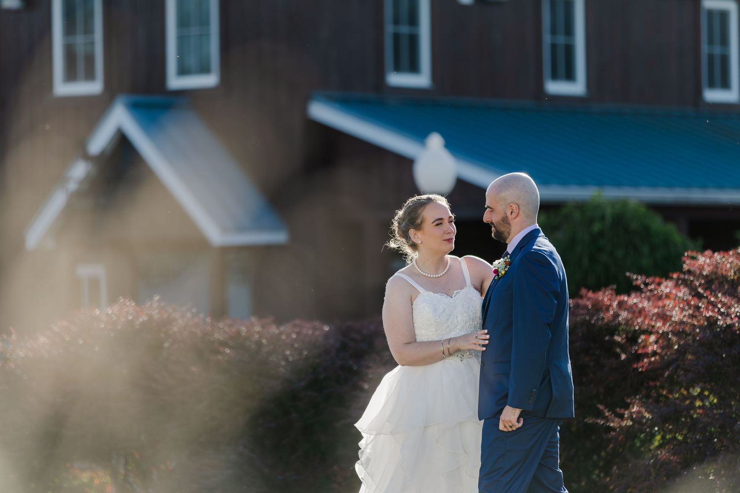 Bride and groom share a quiet moment away from guests in the grass field beside the rustic building of Hauser Hall in Kitchener, Ontario.