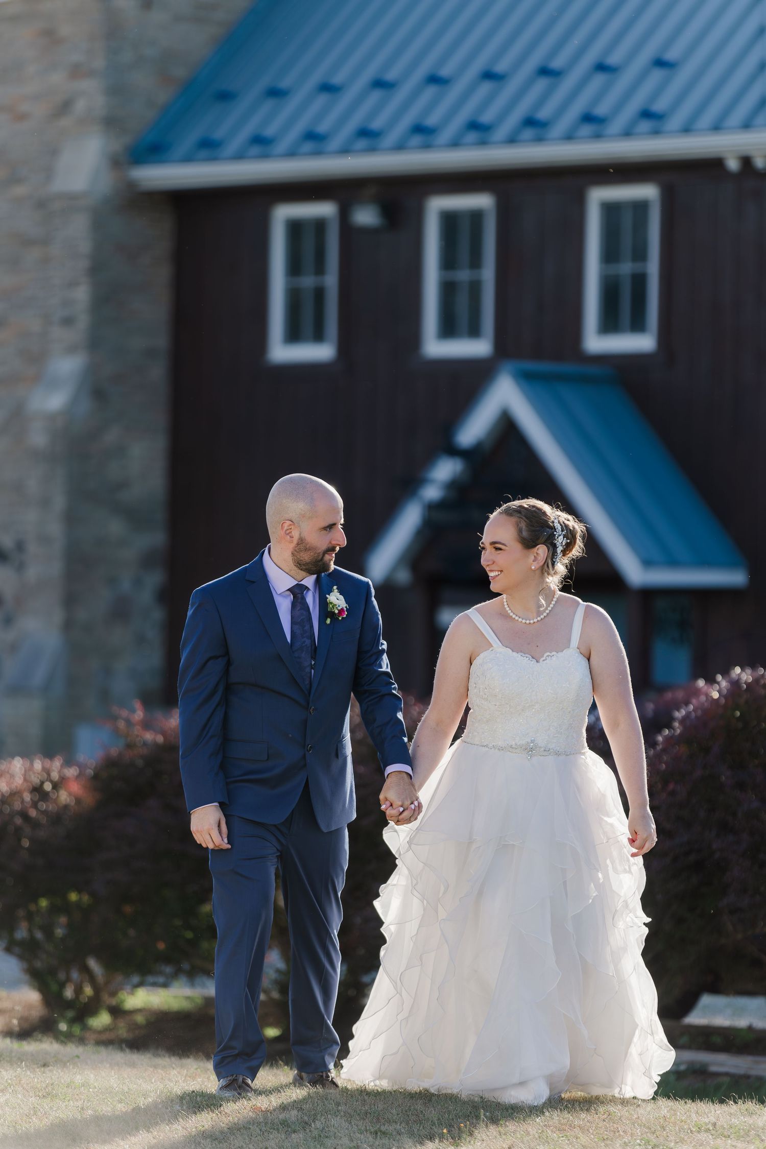 Happy couple walks hand in hand outside the rustic building of Hauser Hall in Kitchener, Ontario.
