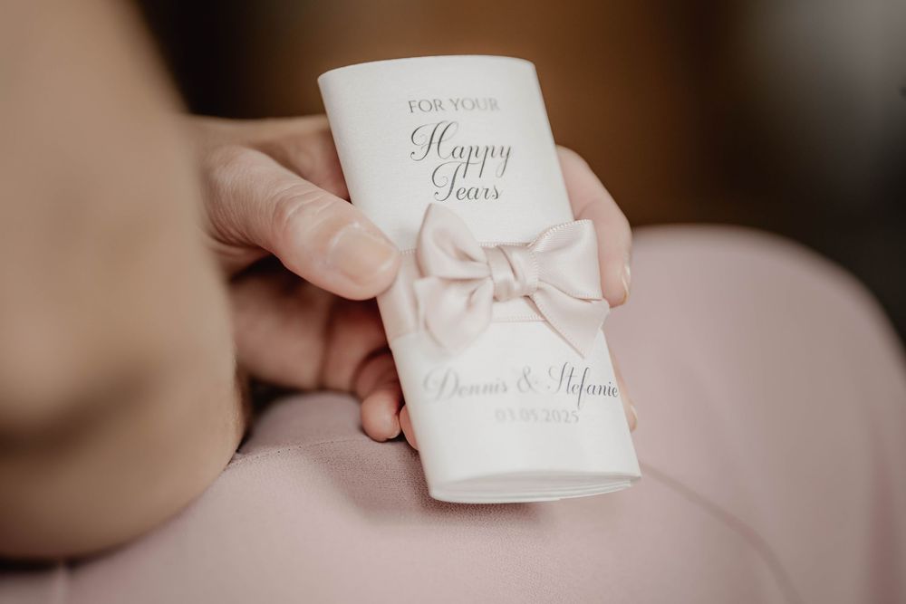 A white wedding program with 'Happy Tears' text and a delicate bow detail.