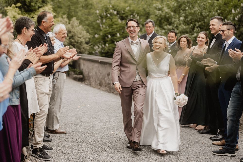 Wedding guests form an aisle, applauding as newlyweds walk through during the celebration.