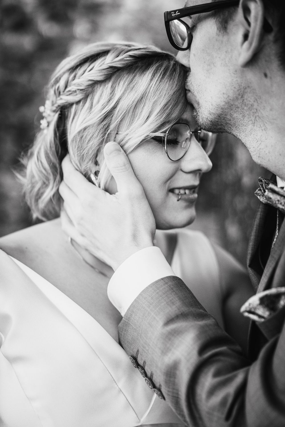 Close-up black and white romantic portrait of a couple embracing and smiling while wearing glasses.