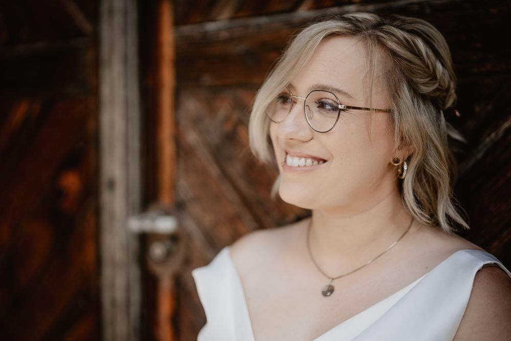 Elegant bridal portraits showing woman in white dress and glasses against rustic wooden background.