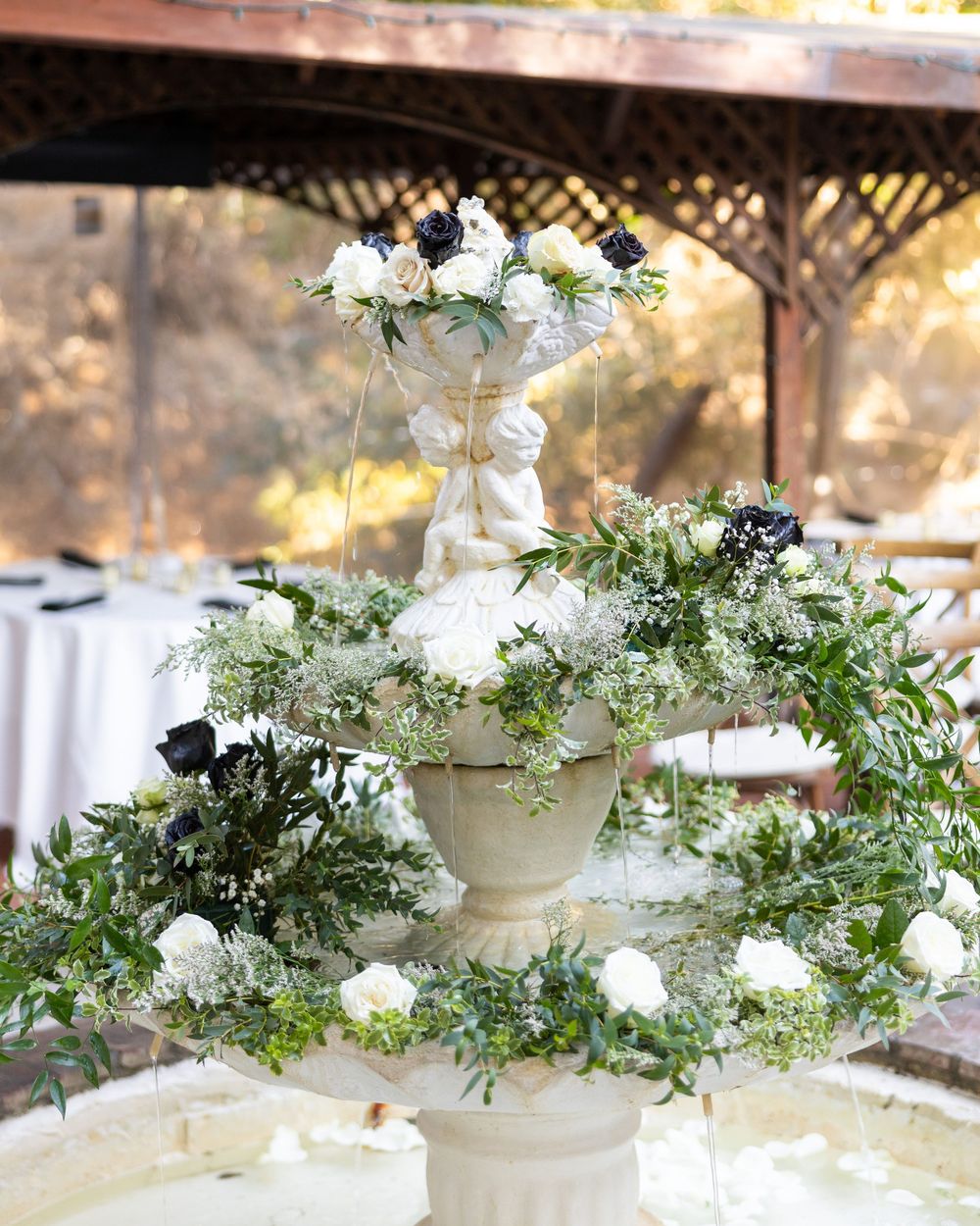 Elegant white floral arrangements with greenery cascading down tiered display stands create a romantic wedding setting.