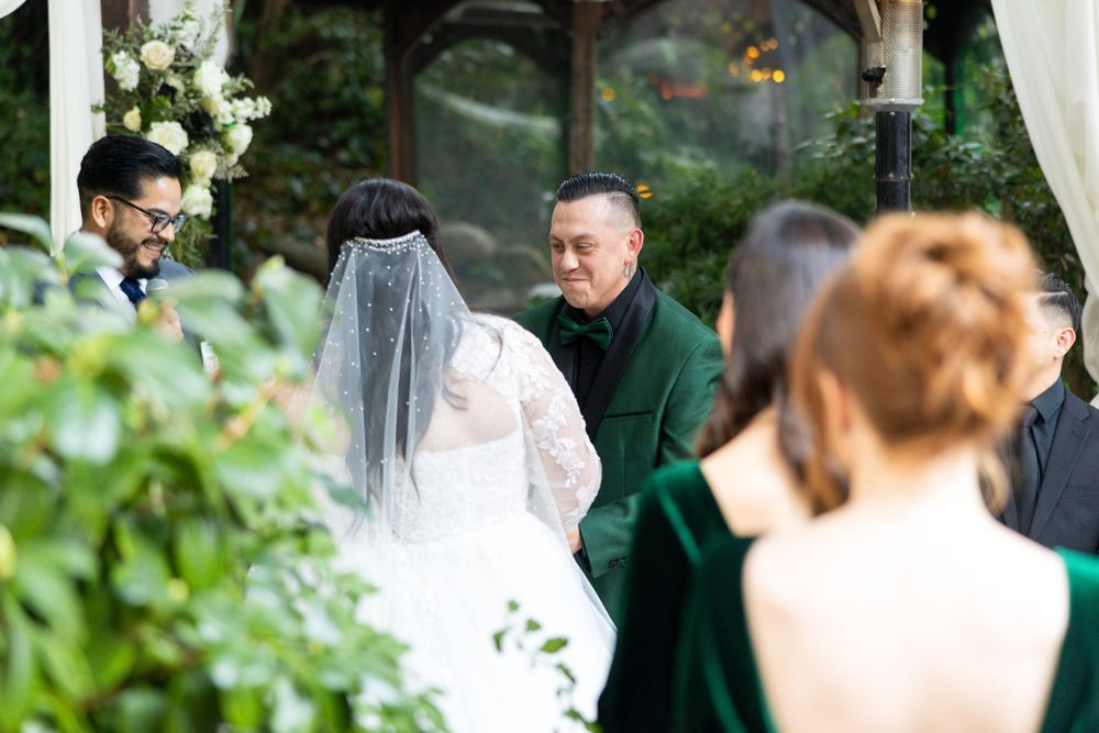 Wedding ceremony under a floral arch with guests gathered in a lush outdoor garden setting.