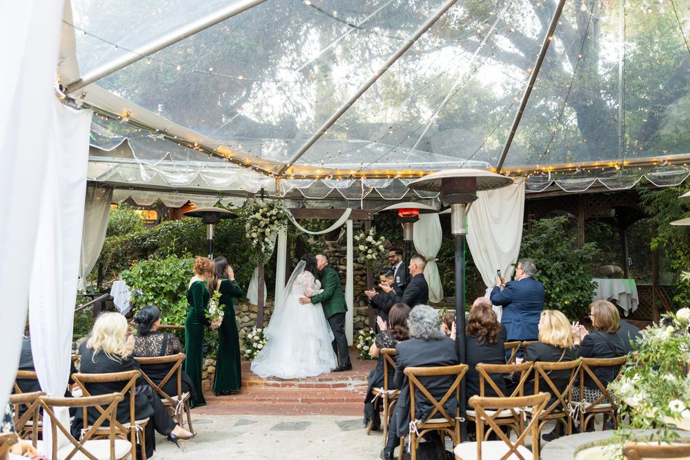 Wedding reception setup under white tents with wooden chairs and tables arranged outdoors.