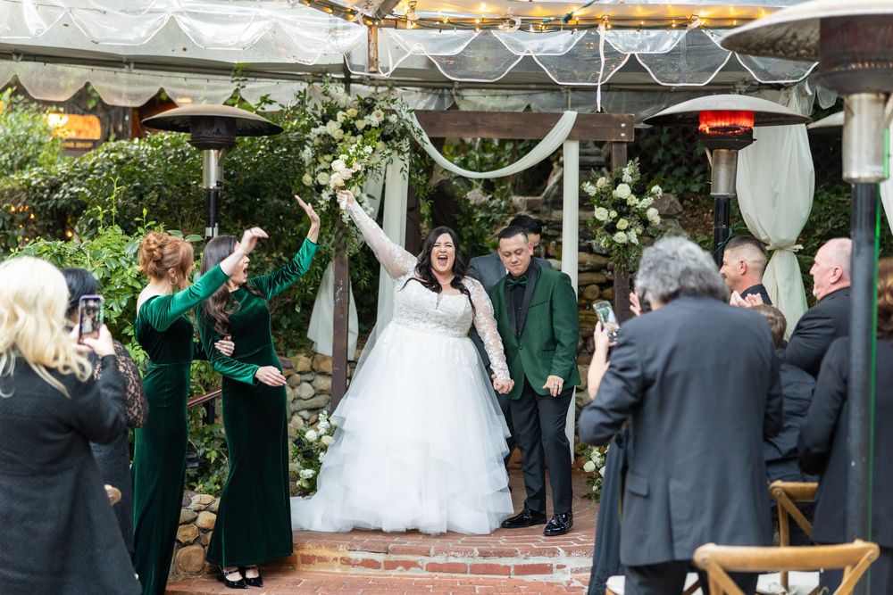 Outdoor wedding ceremony setup with white chairs and floral arrangements under a rustic wooden pavilion.