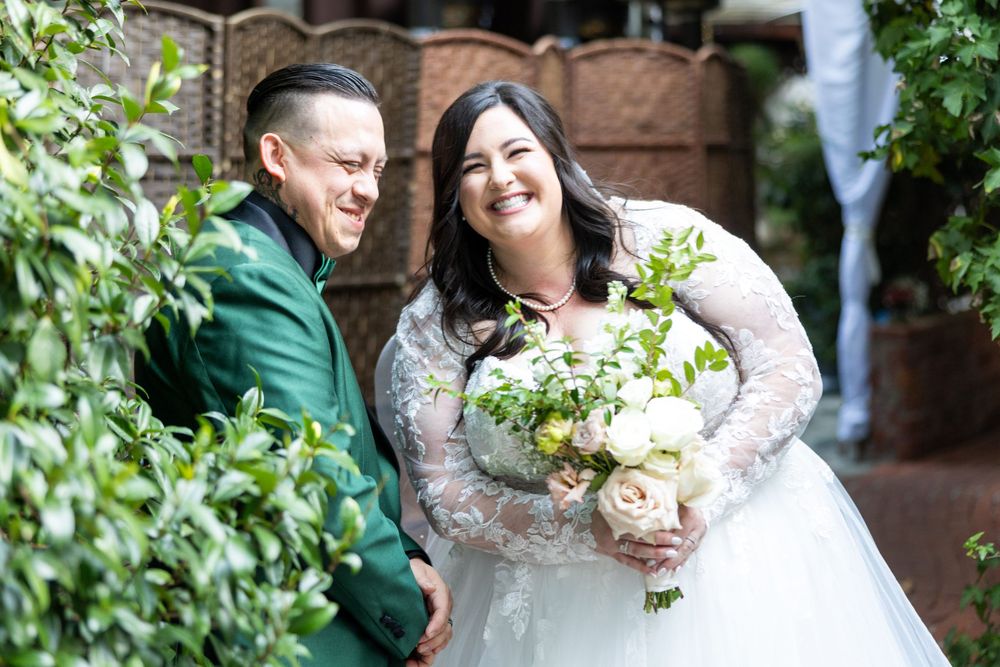 A bride and groom share a joyful embrace while posing for wedding portraits in a garden setting.