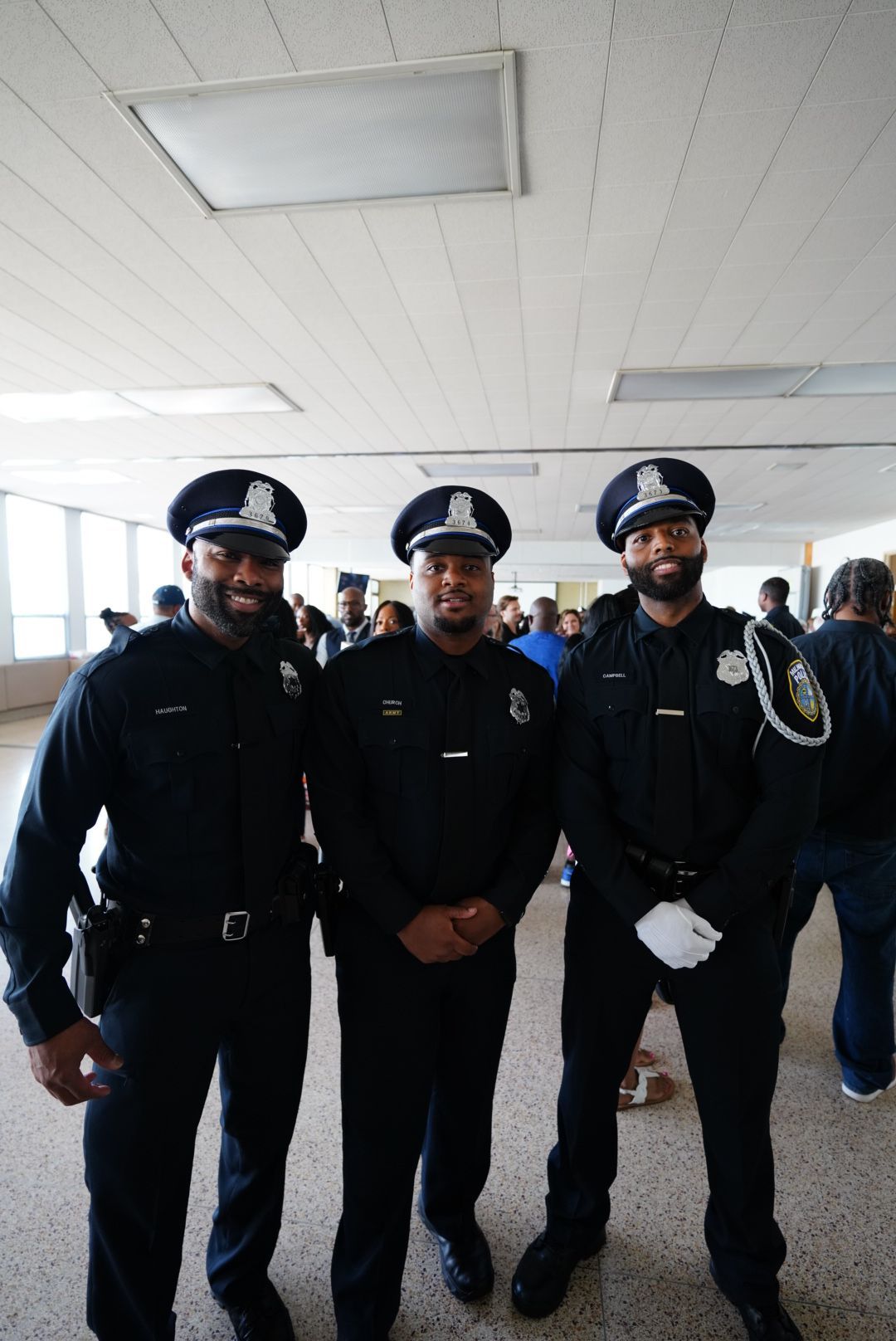 Three police officers in uniform stand together smiling in a hallway.
