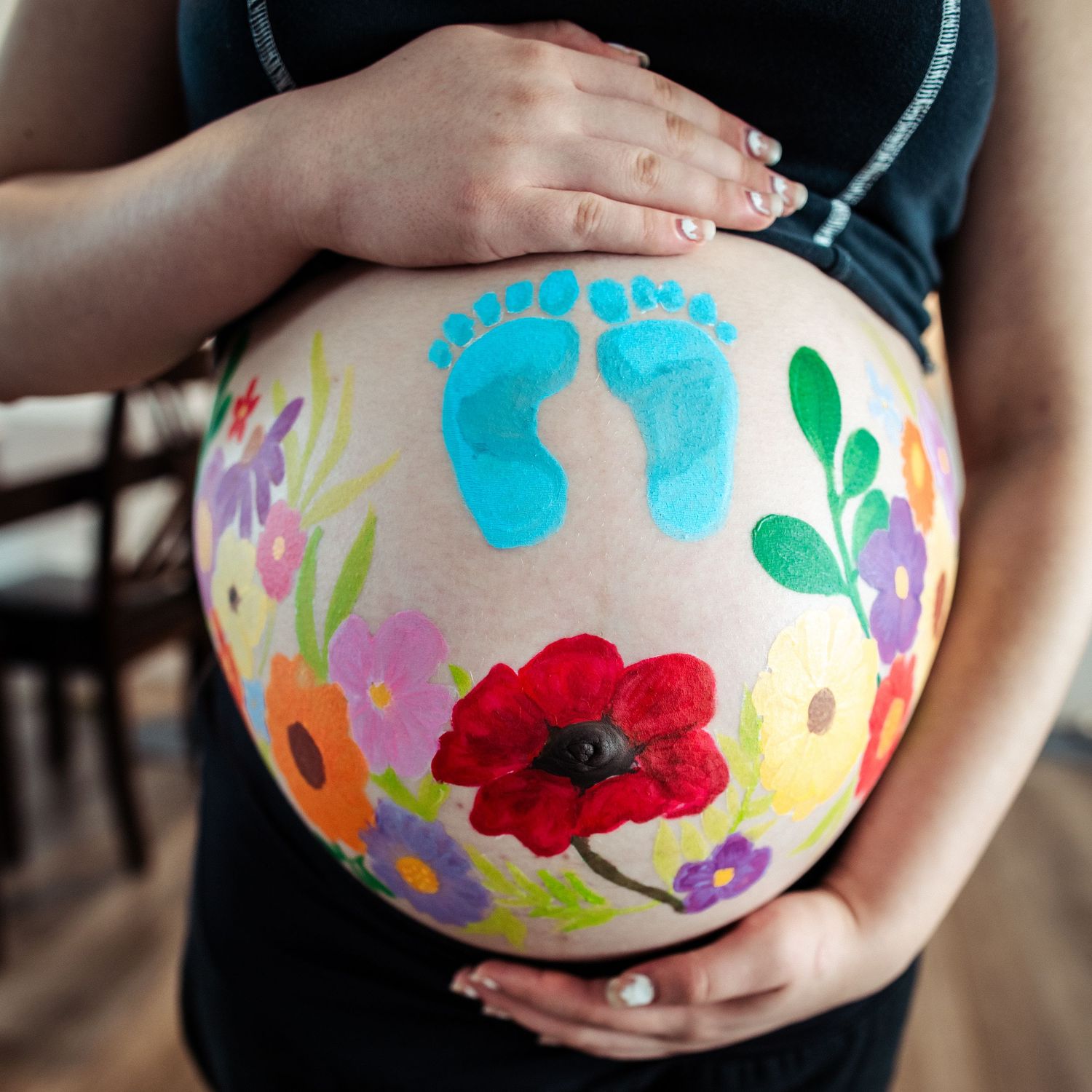 Colorful floral designs painted on a pregnant belly against dark clothing.