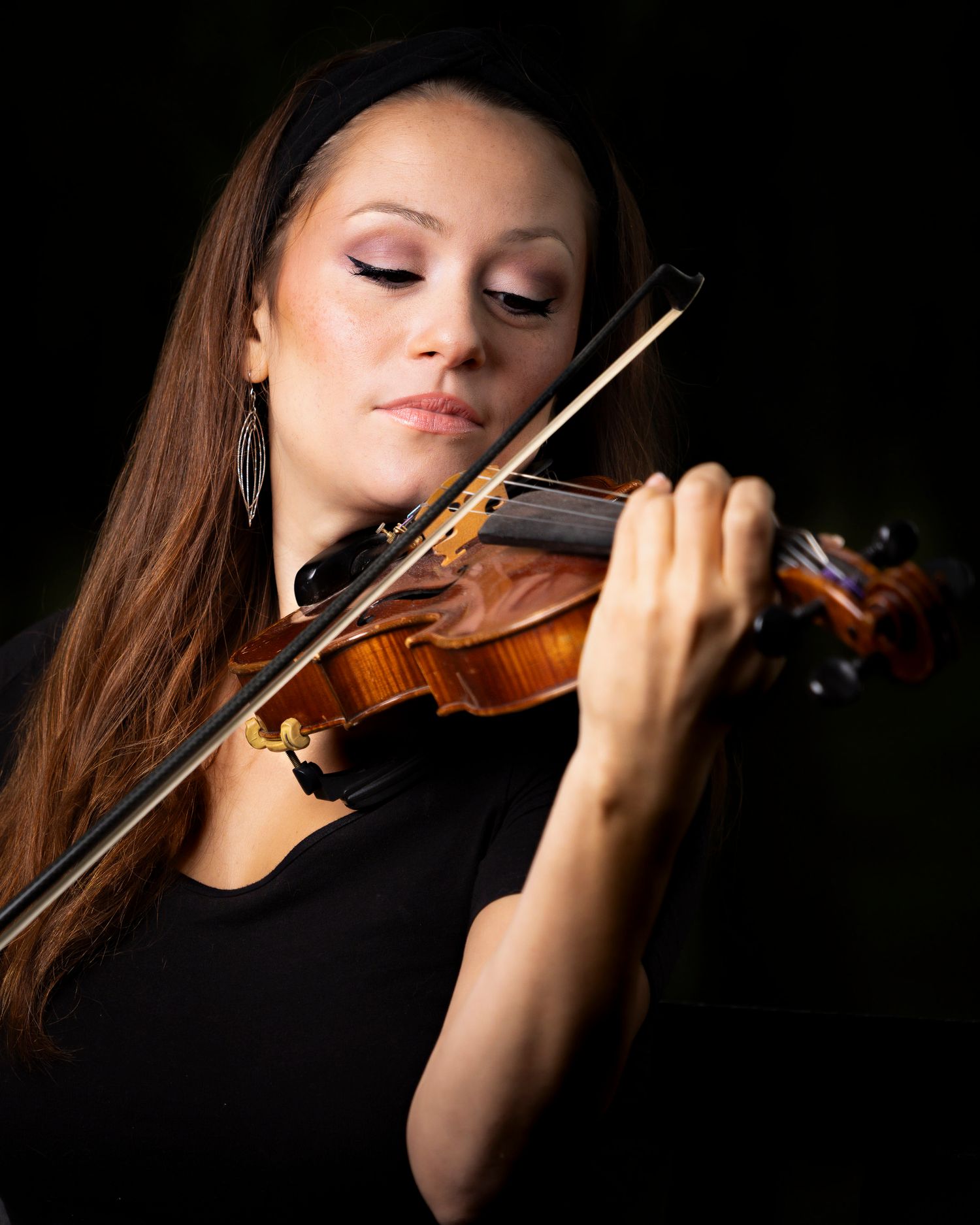 A violinist performs in dramatic lighting while playing classical music with focused concentration.