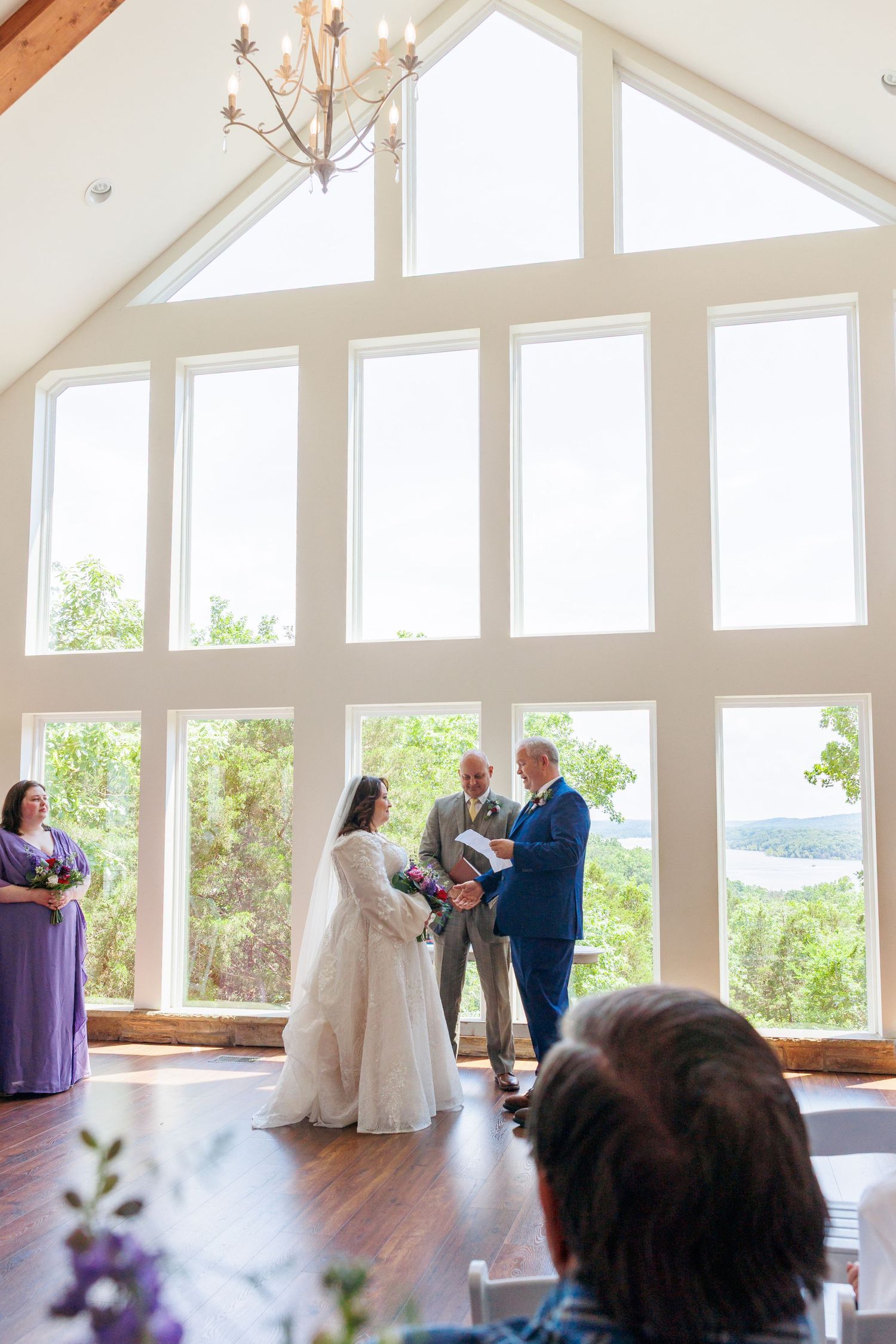 Panoramic view of a wedding ceremony in a bright sunlit room with vaulted ceilings and large windows overlooking nature on Table Rock Lake.