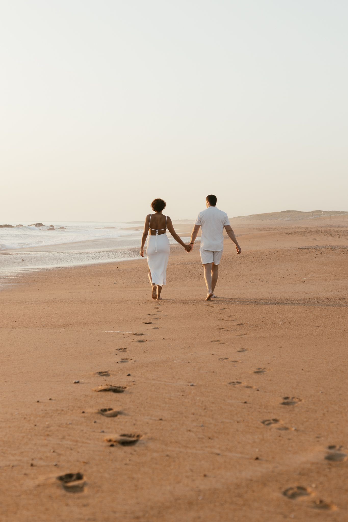 Couple jeune et amoureux sur la plage en Vendée, photographié dans une ambiance lumineuse et poétique au coucher du soleil.