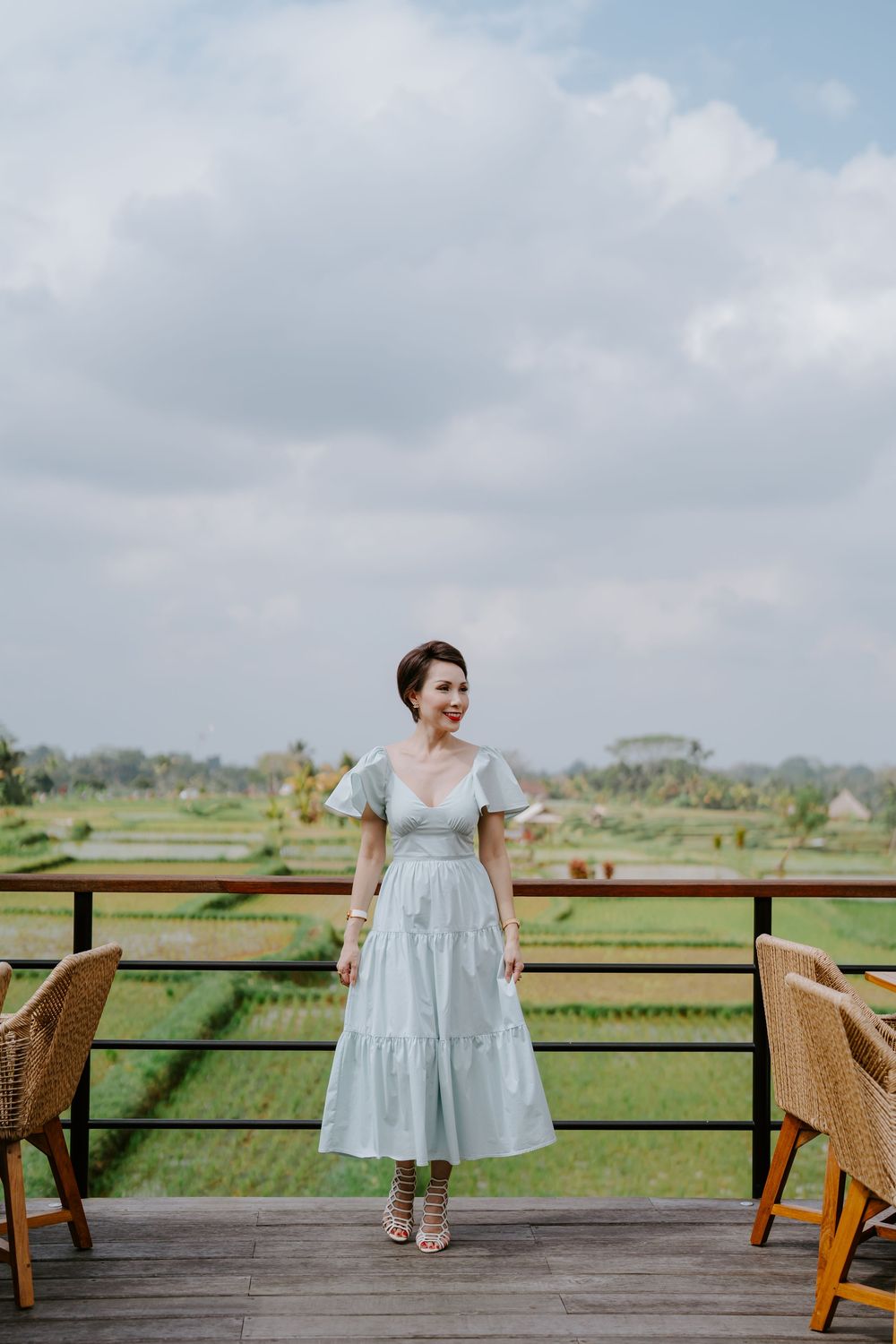 A light blue dress photoshoot on a wooden deck overlooking green rice fields.