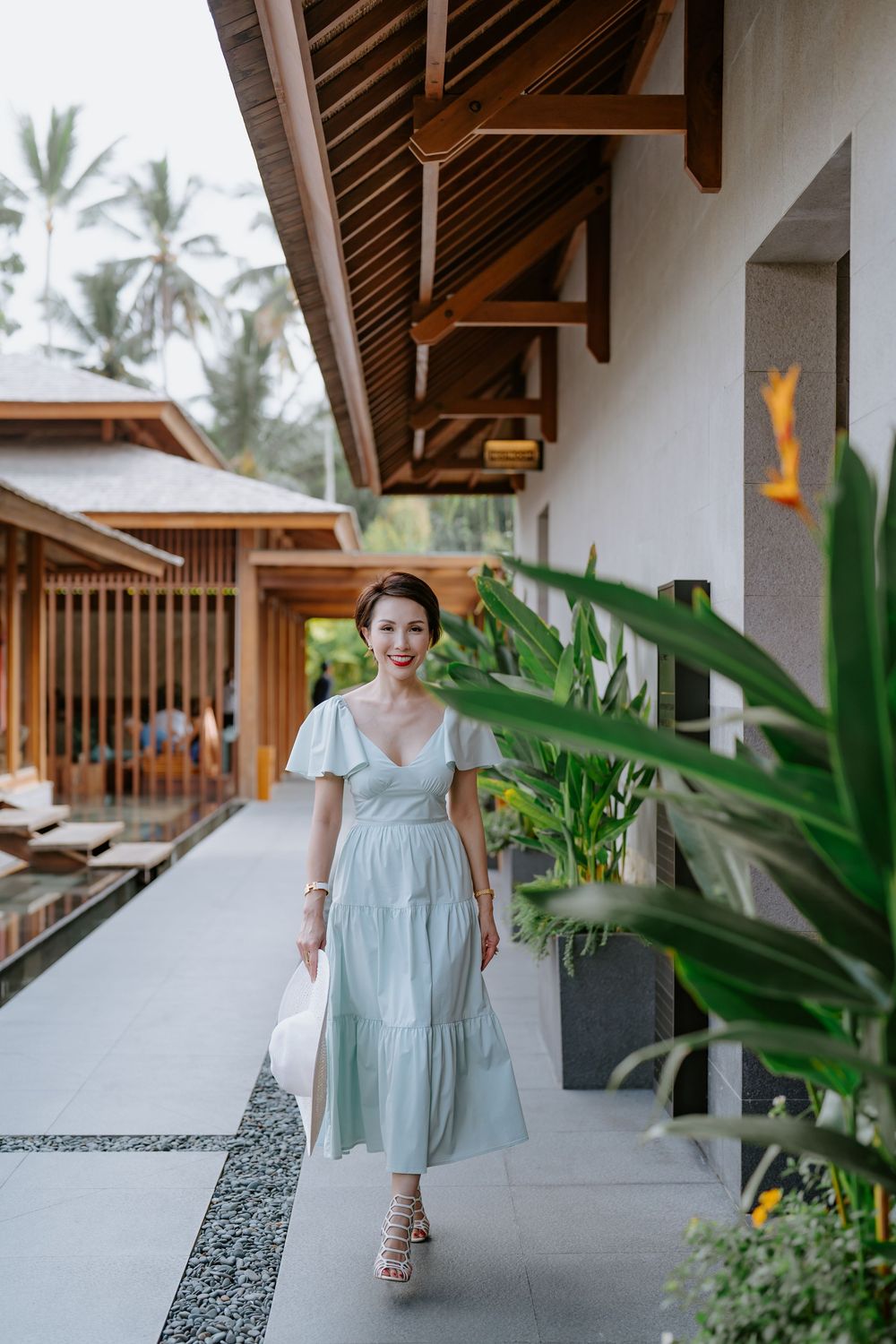 A light blue dress photoshoot along a modern villa corridor with tropical plants.