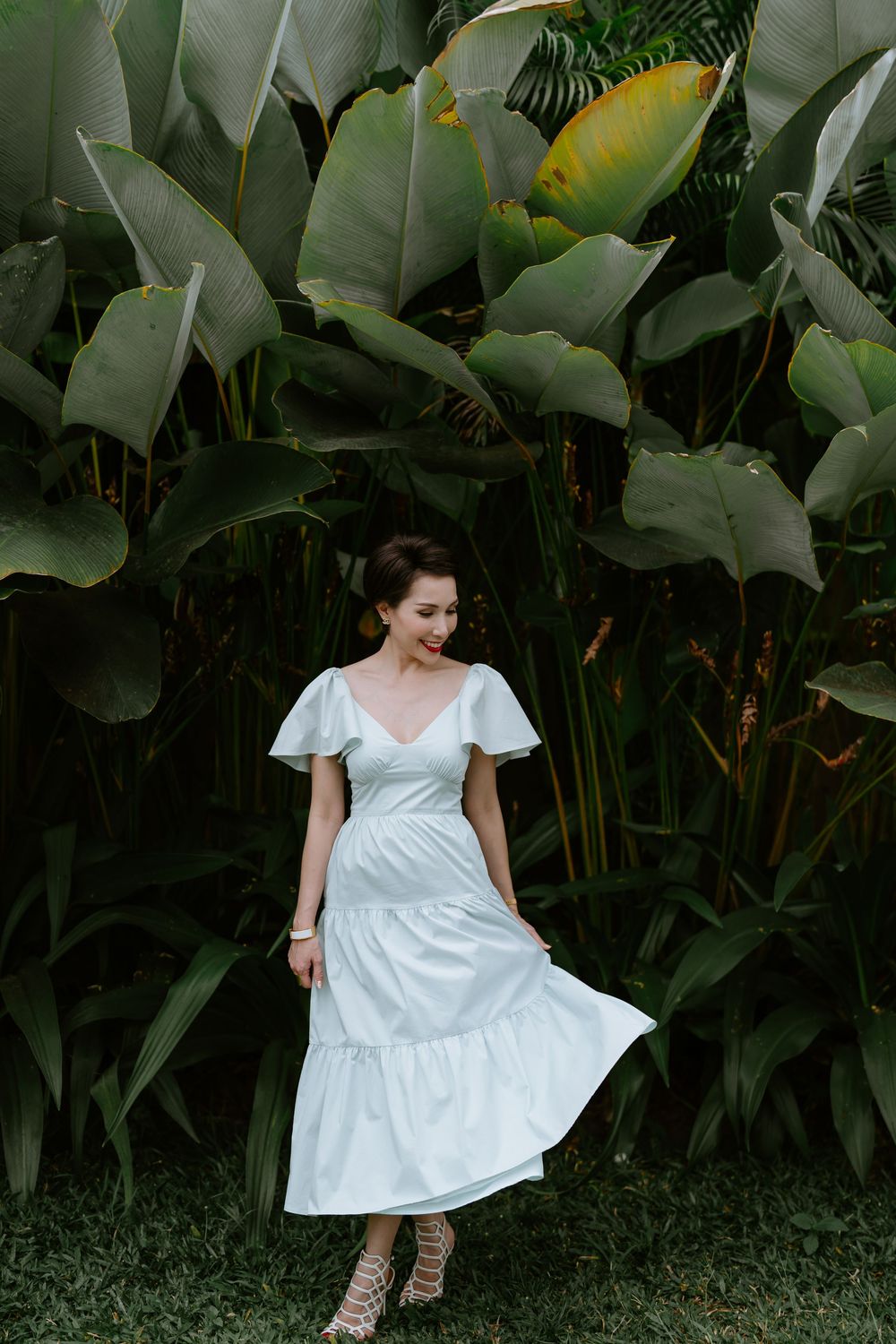 A white summer dress twirls against a backdrop of large tropical leaves and greenery.