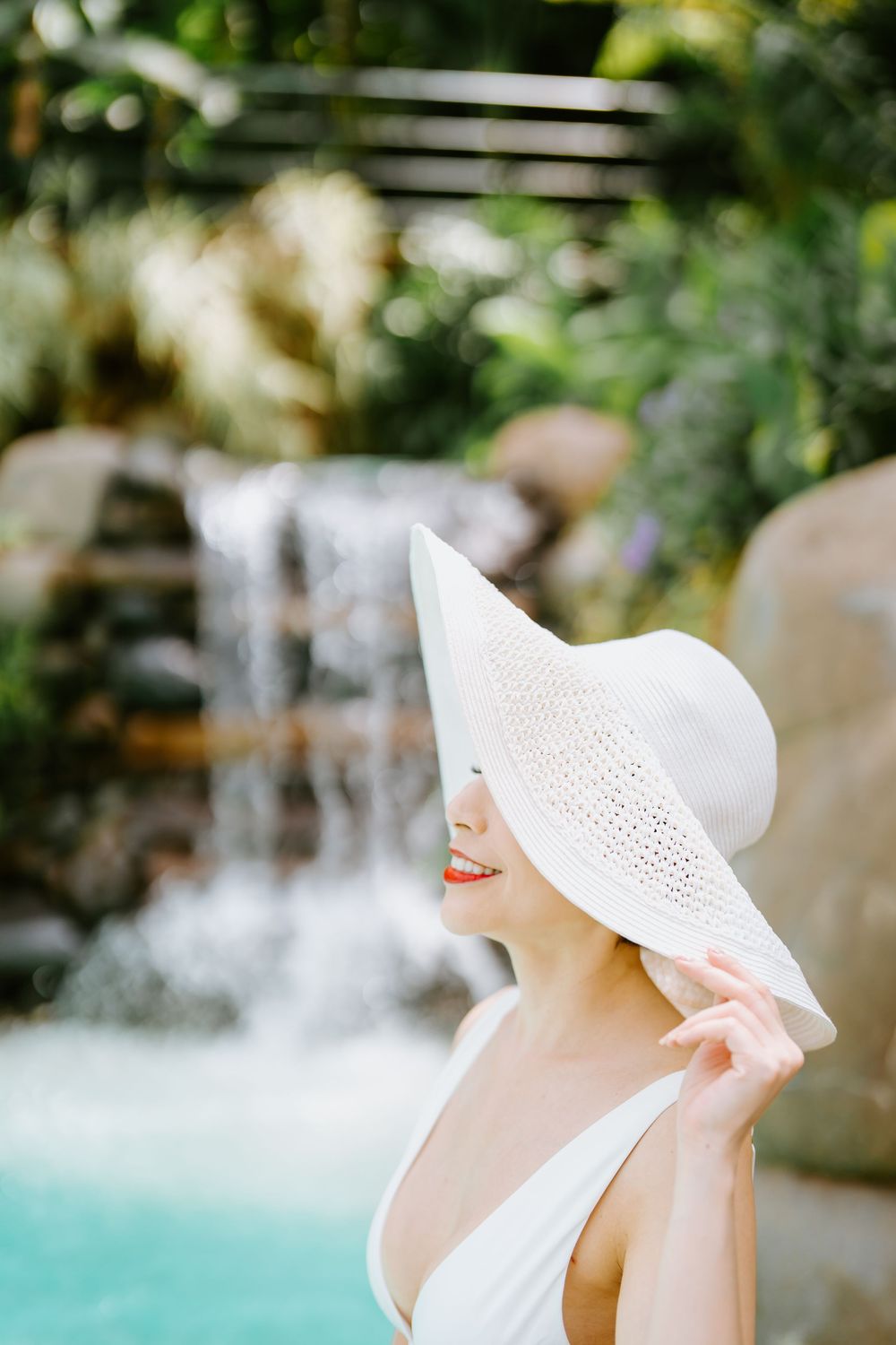 A white sunhat frames a profile view against a blurred waterfall background.