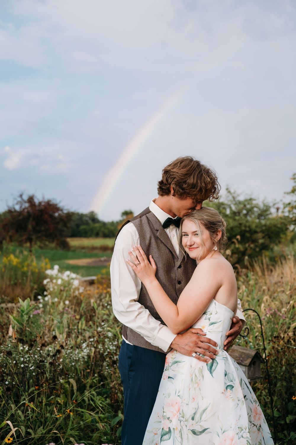 Groom & bride embracing in Lowe Park Marion Iowa under rainbow taken by Iowa midwest wedding photographer